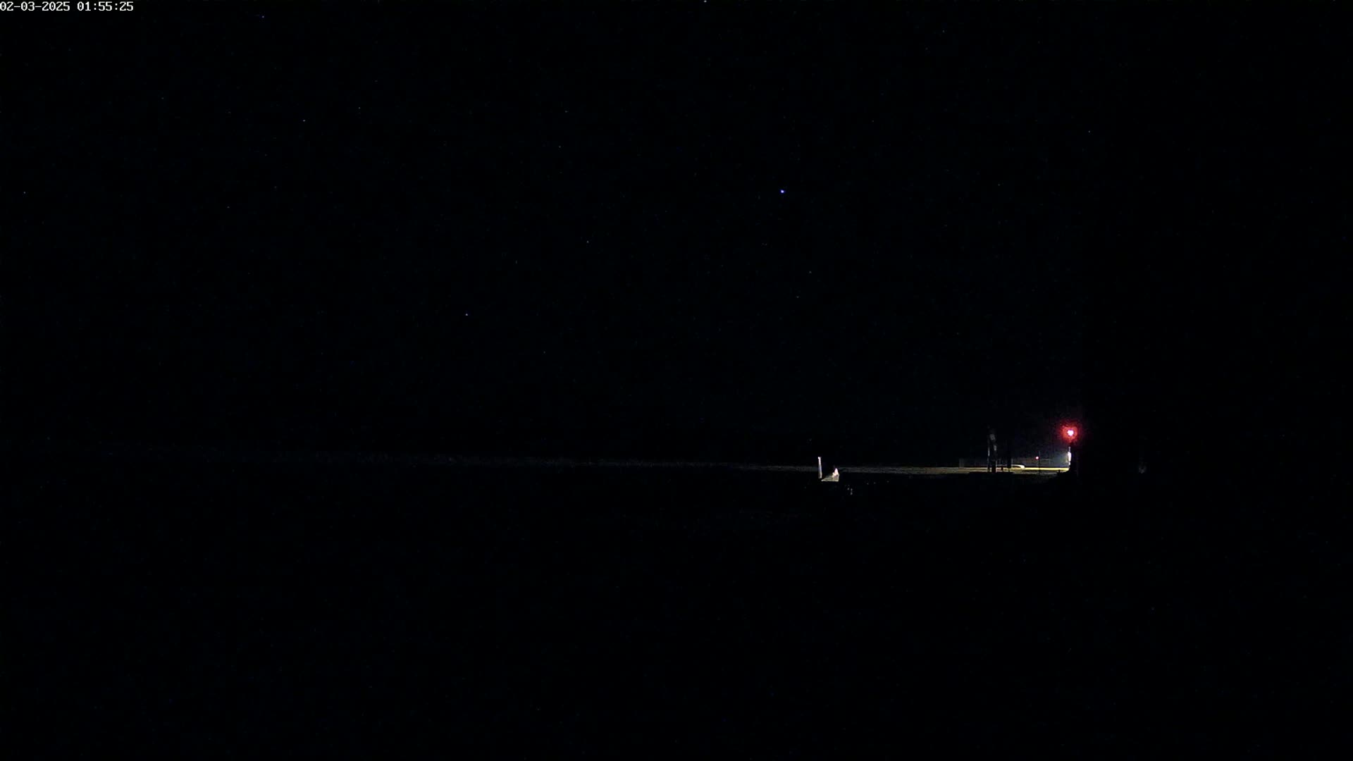 Two figures stand near a faintly lit area under a dark, clear night sky dotted with stars.