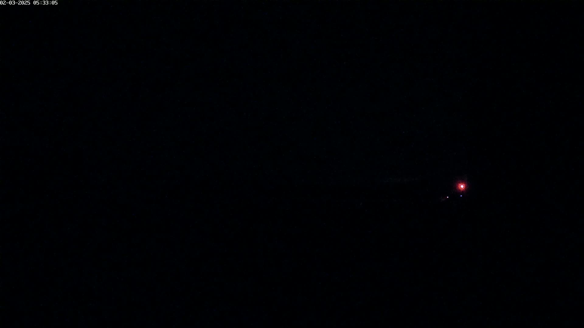 A small, faint red light is visible in the center of a completely dark, nighttime scene.