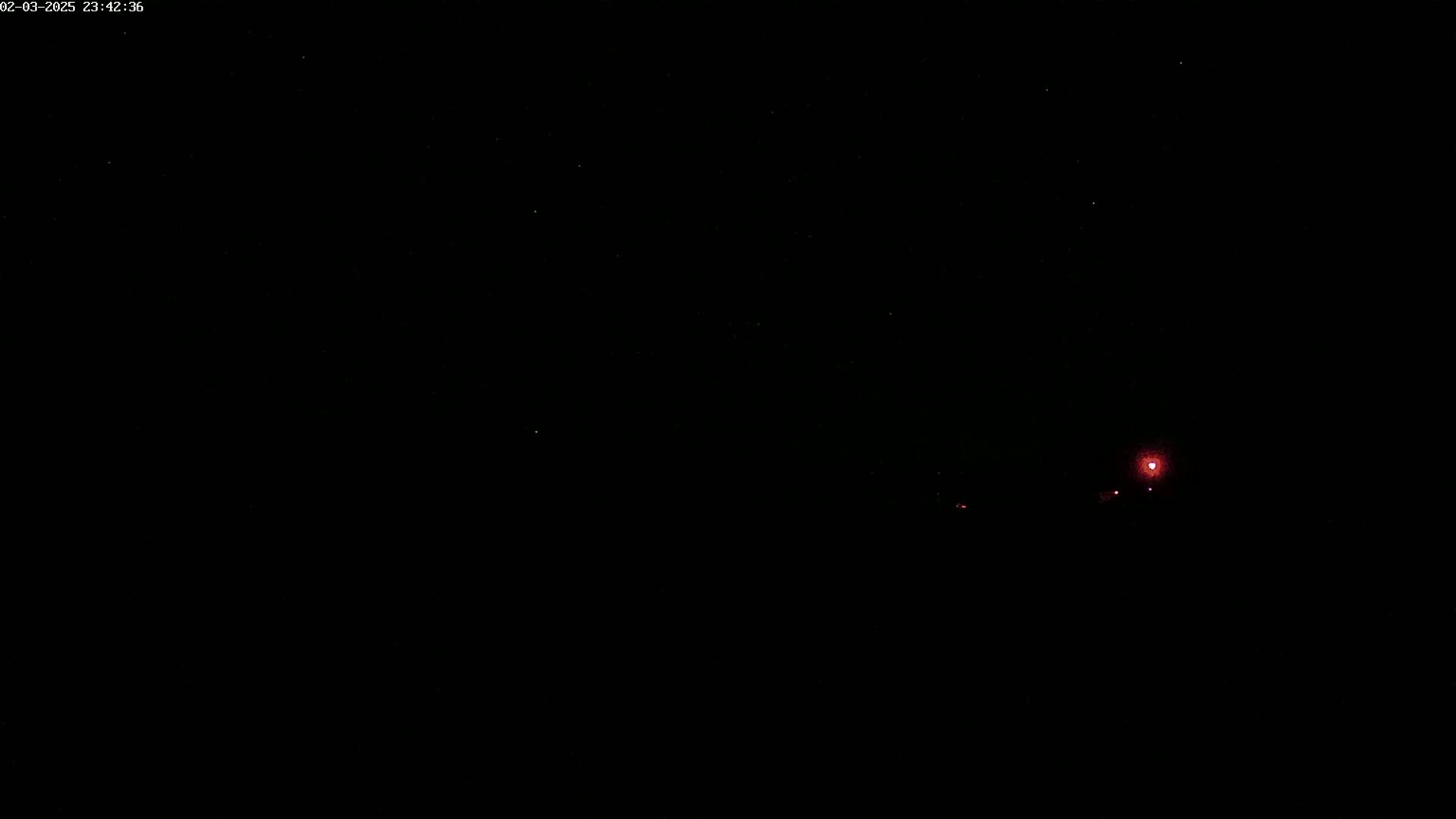 A nighttime scene shows a faint, reddish light in the distance under a dark, star-filled sky.
