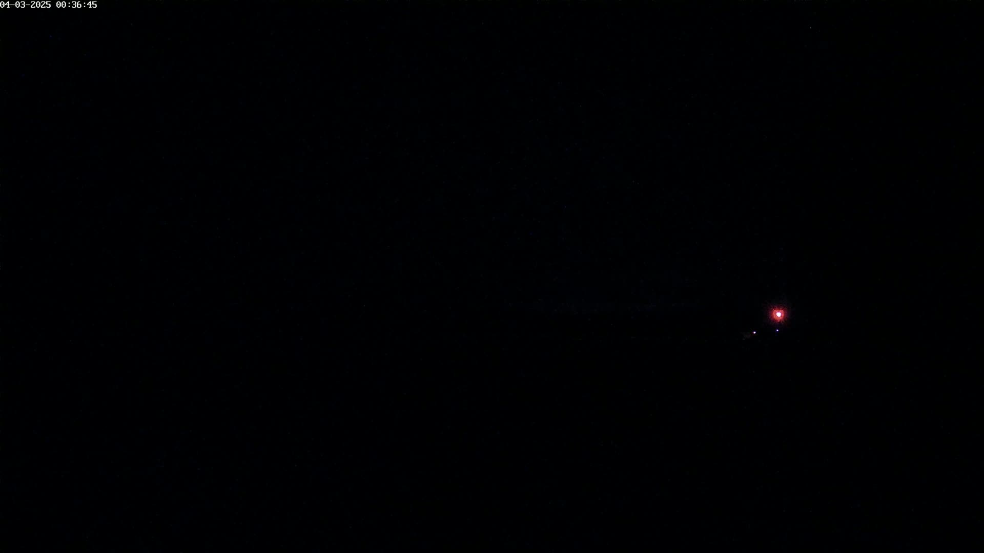 A small, faint red light is visible in the distance against a completely dark, nighttime sky.
