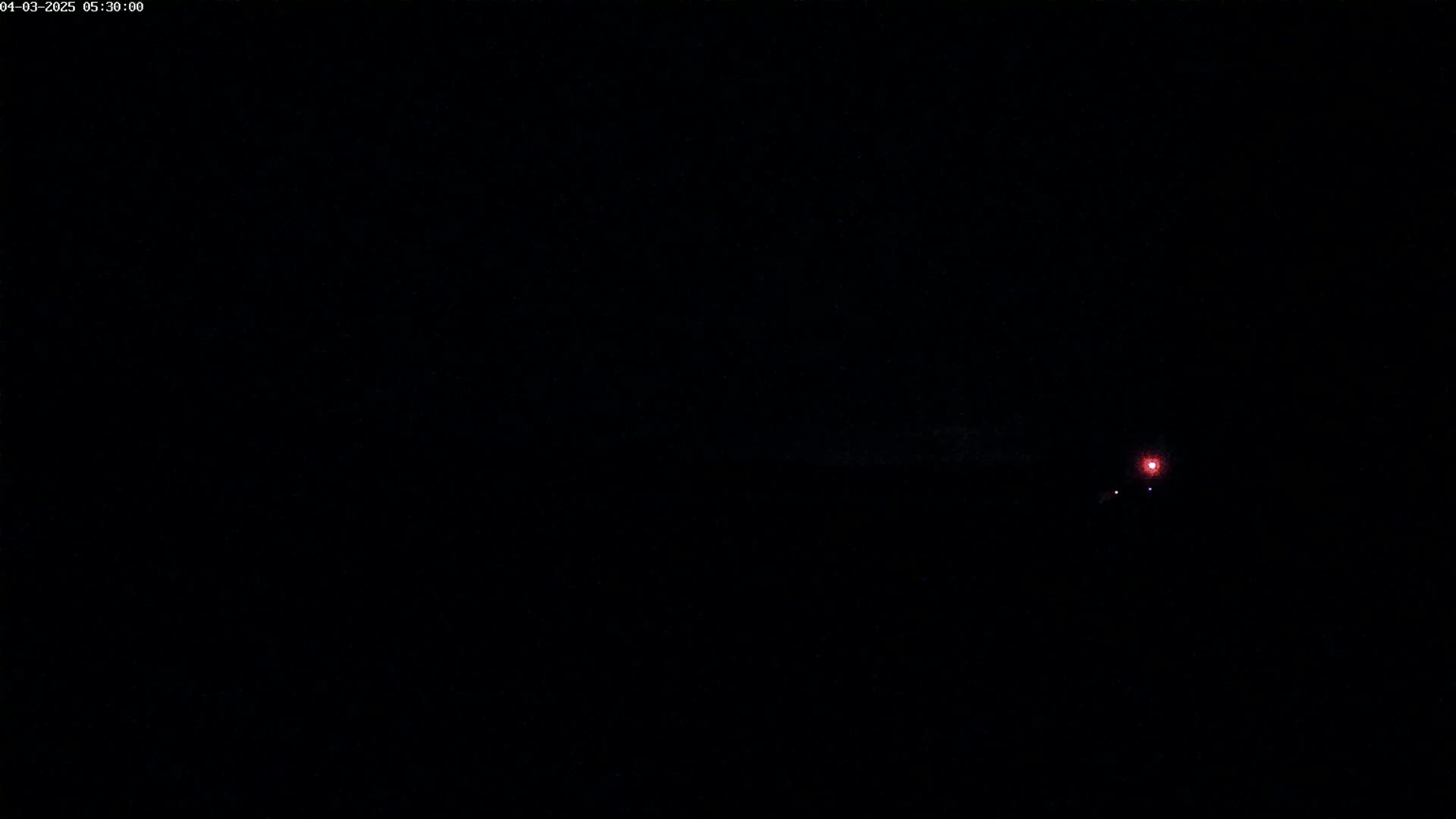 A small, faint red light is visible in the distance against a completely dark night sky.