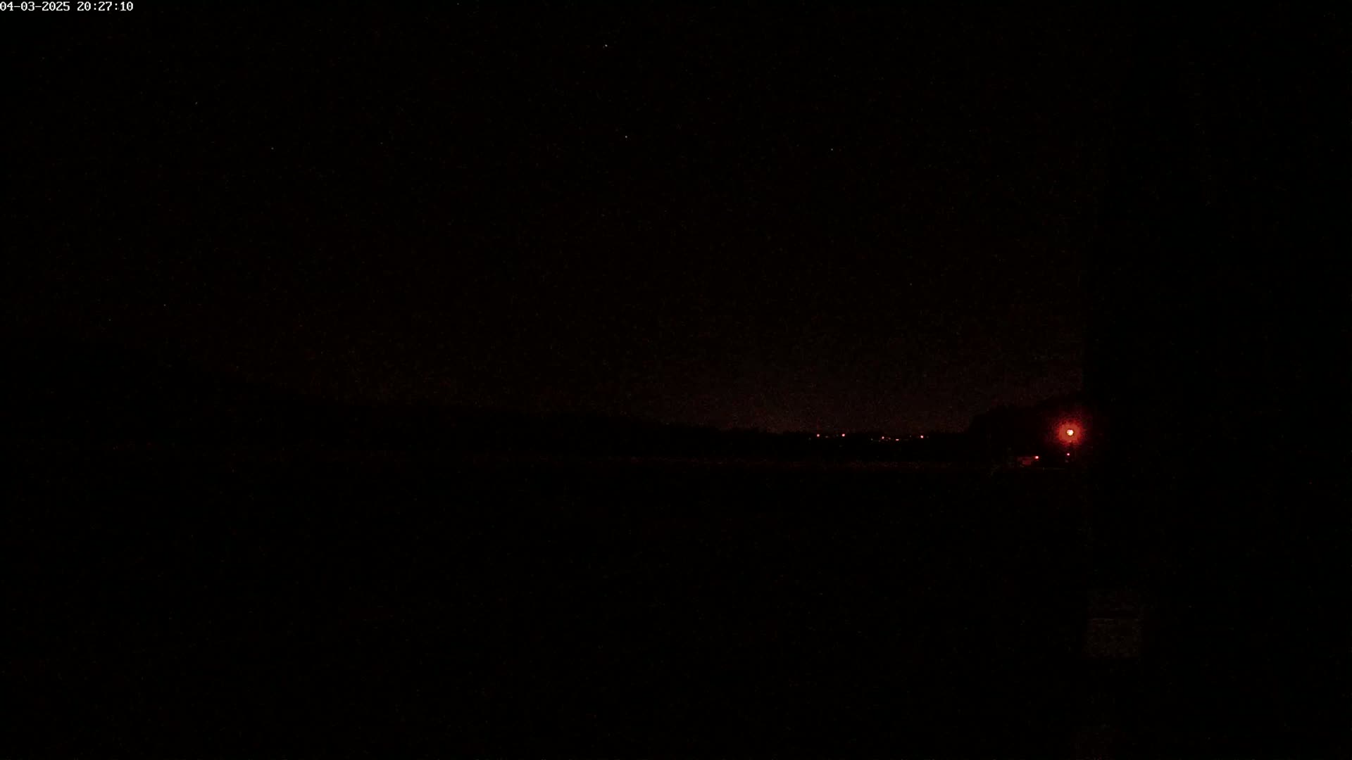 A dark, nighttime scene shows a distant line of faint lights on the horizon under a clear, starlit sky.