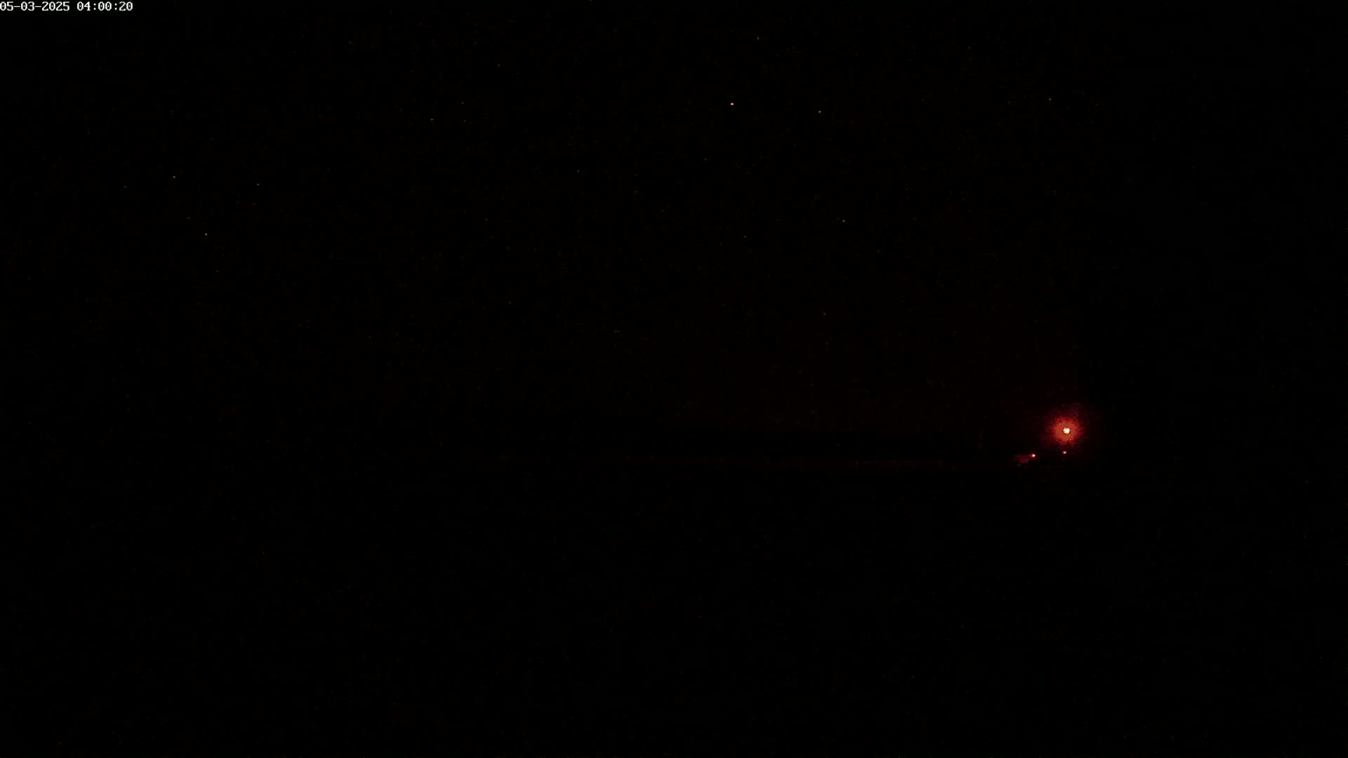 A dark night sky with a few visible stars and a small, distant red light on the horizon.