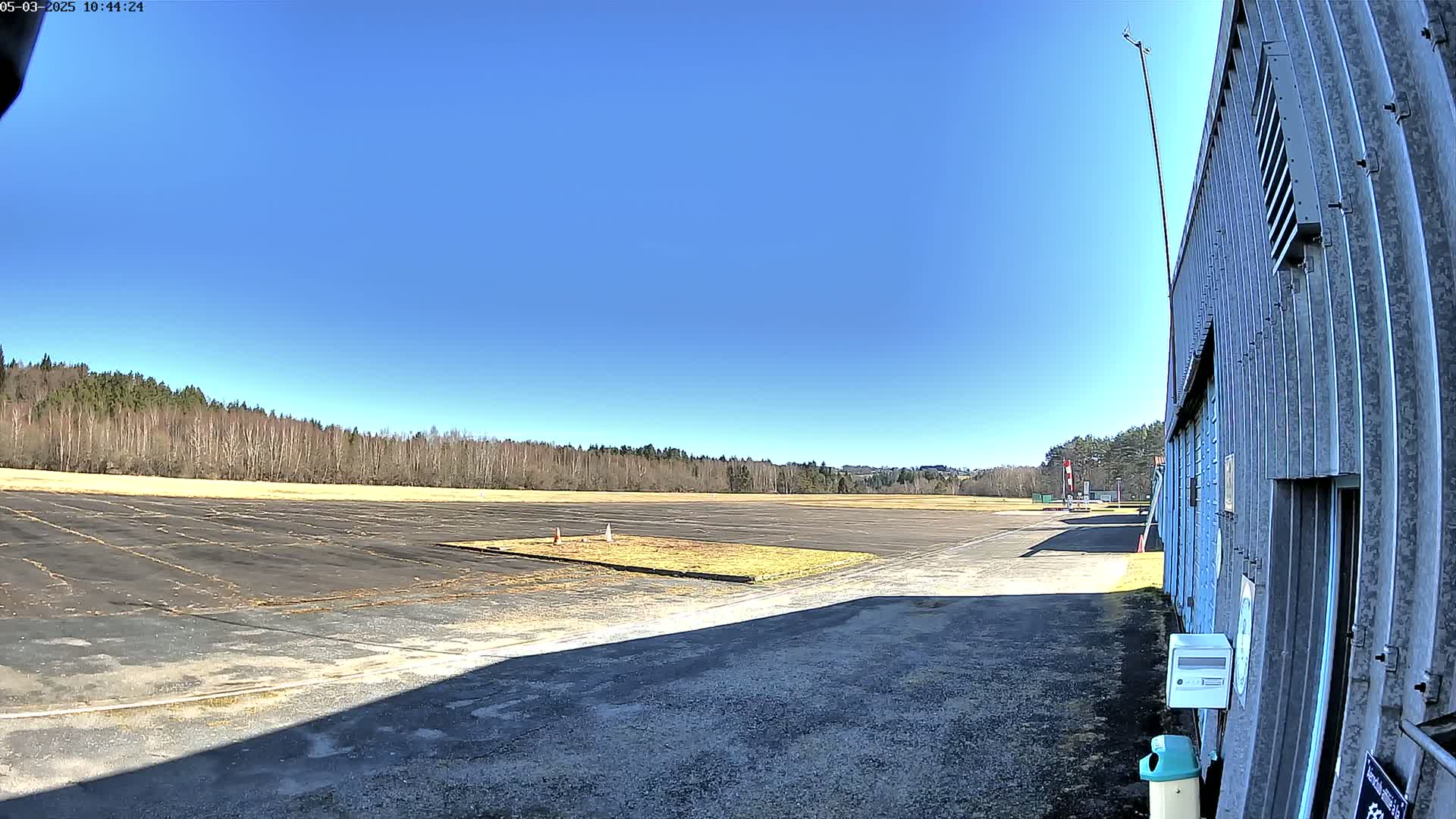A paved airfield stretches toward a line of leafless trees under a clear blue sky.