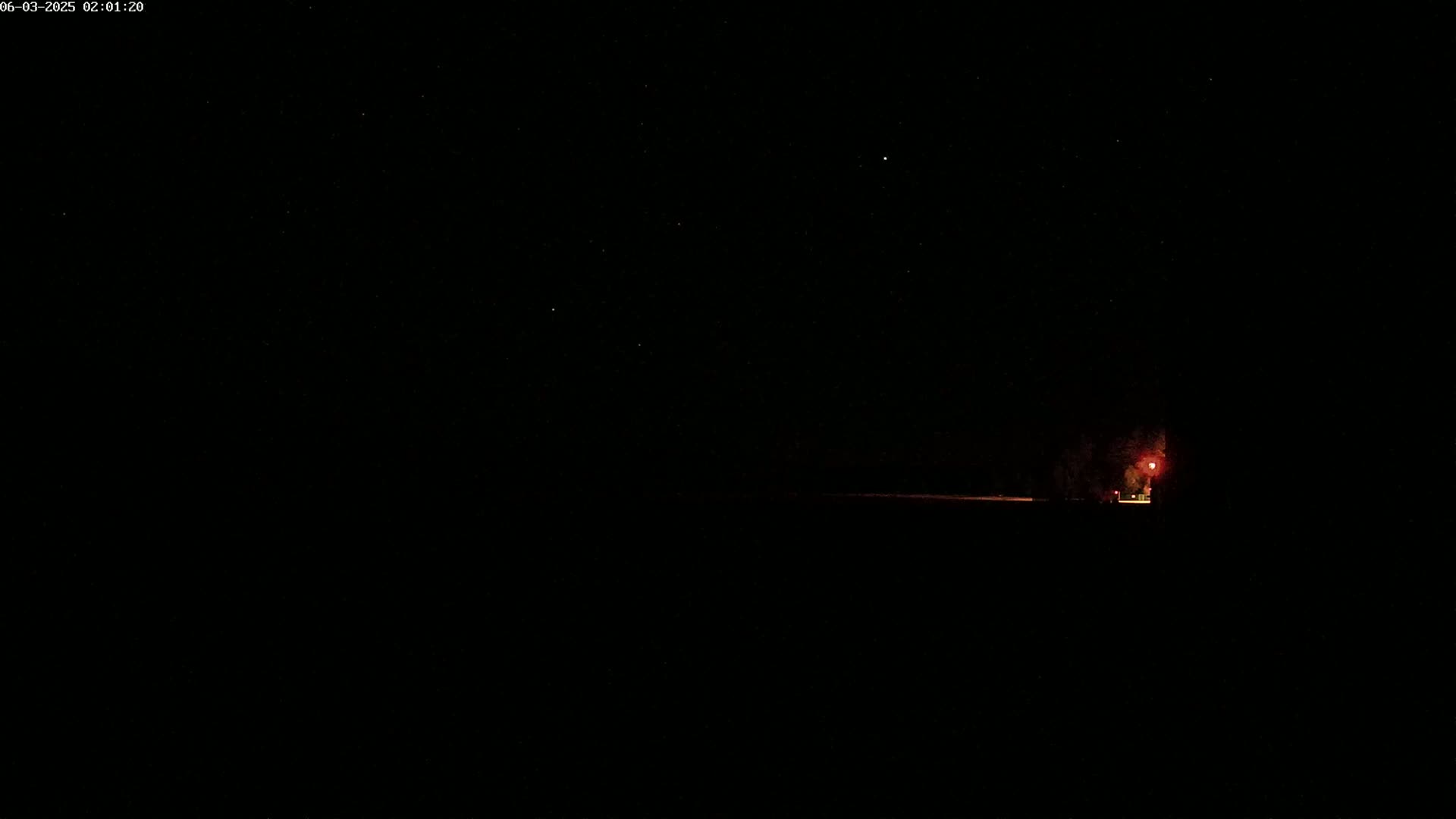 A dark, nighttime scene shows a faint, reddish light in the distance under a clear, starry sky.