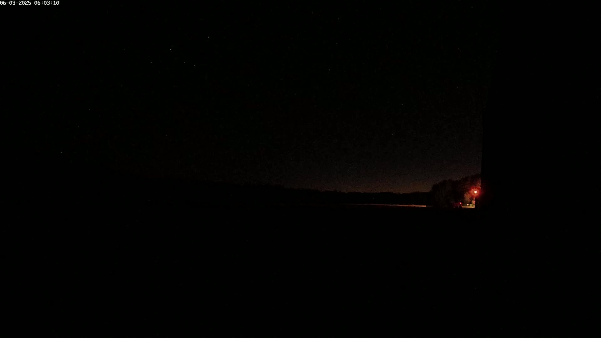 A dark, nighttime scene shows a distant, dimly lit horizon and a single light source to the right, under a mostly clear, star-filled sky.