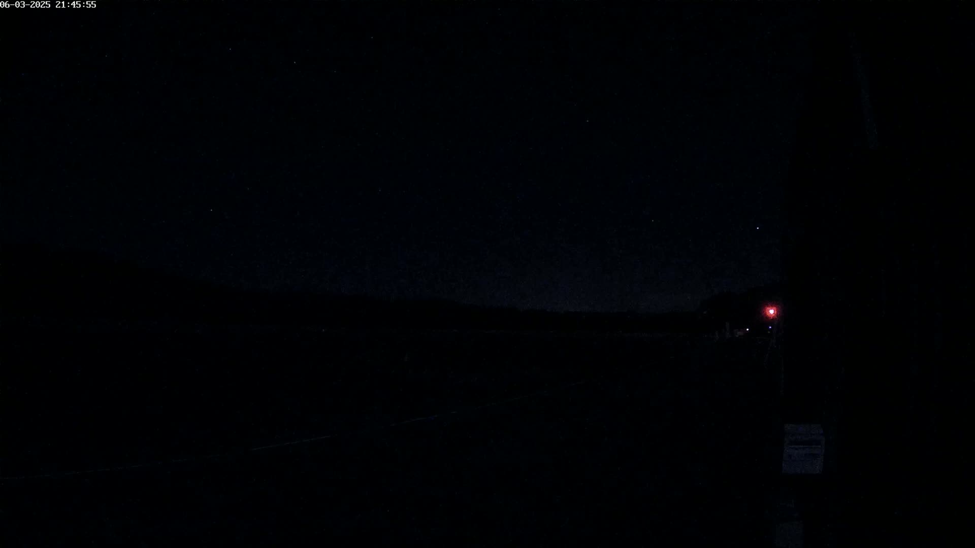 A dark, nighttime scene shows a few stars in the sky above a flat, dark landscape with a faint red light in the distance.