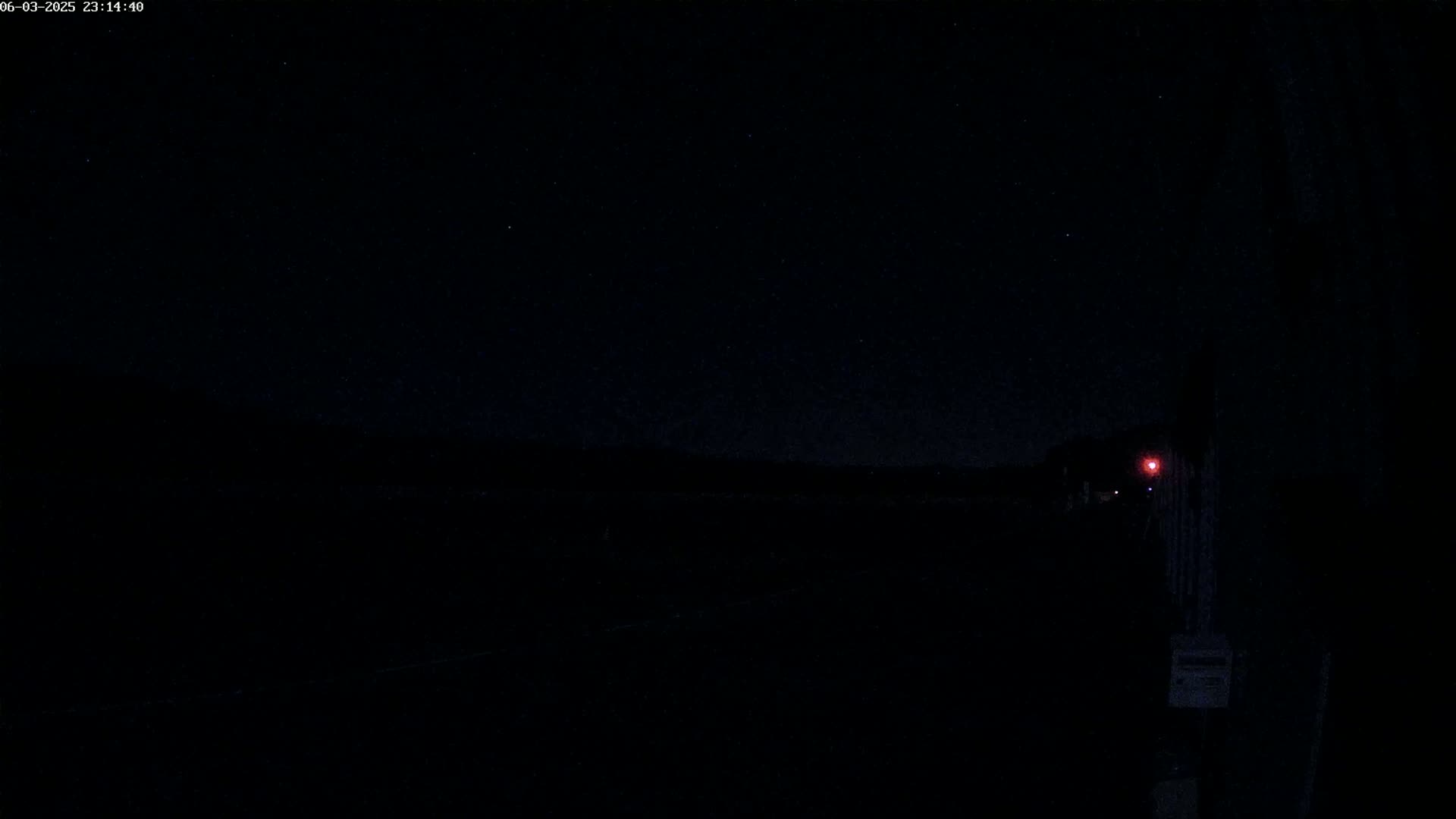 A dark, starlit night scene shows a dimly lit area with a faint red light in the distance.