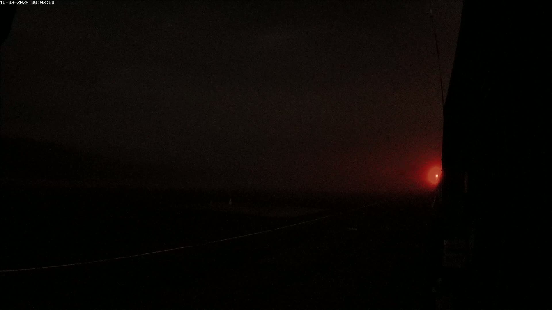 A dark, foggy landscape at night is illuminated by a single, distant red light.