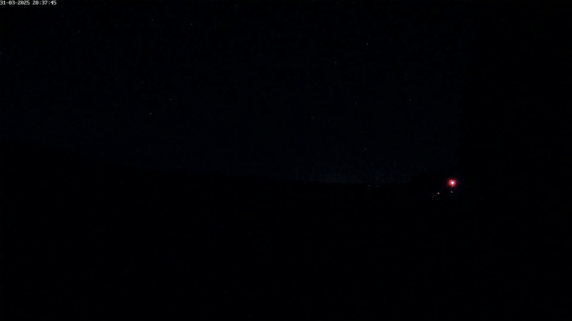 A dark, nighttime scene shows a faint, distant light source on the right and a starry sky above a dark landscape.