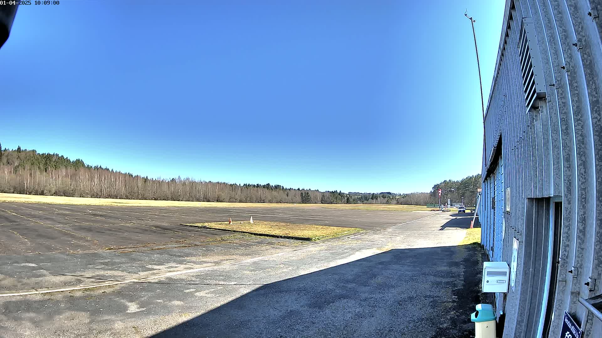 A large, empty tarmac area bordered by trees under a clear blue sky.
