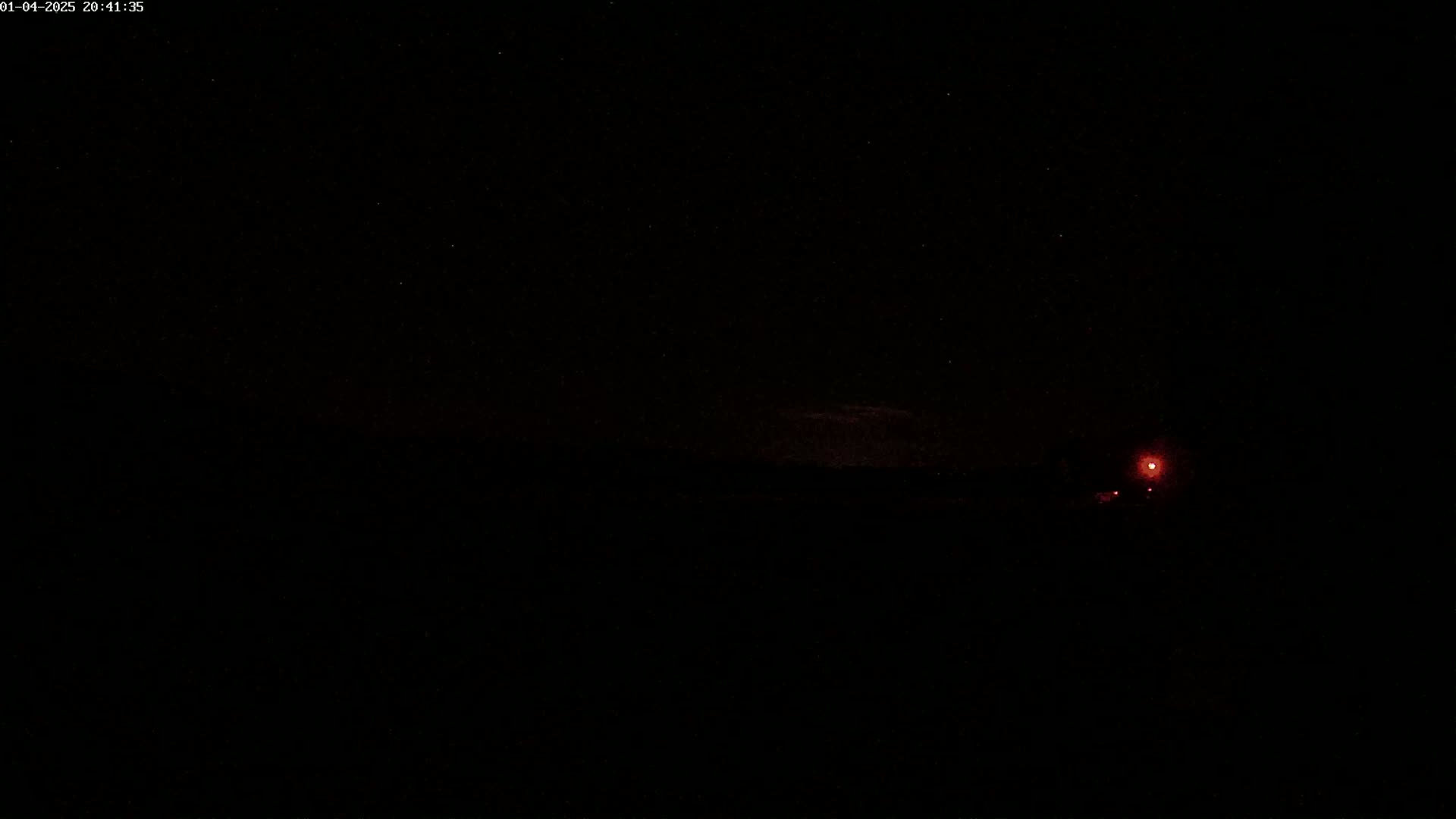 A dark, nighttime scene shows a faint red light in the distance under a starry sky.