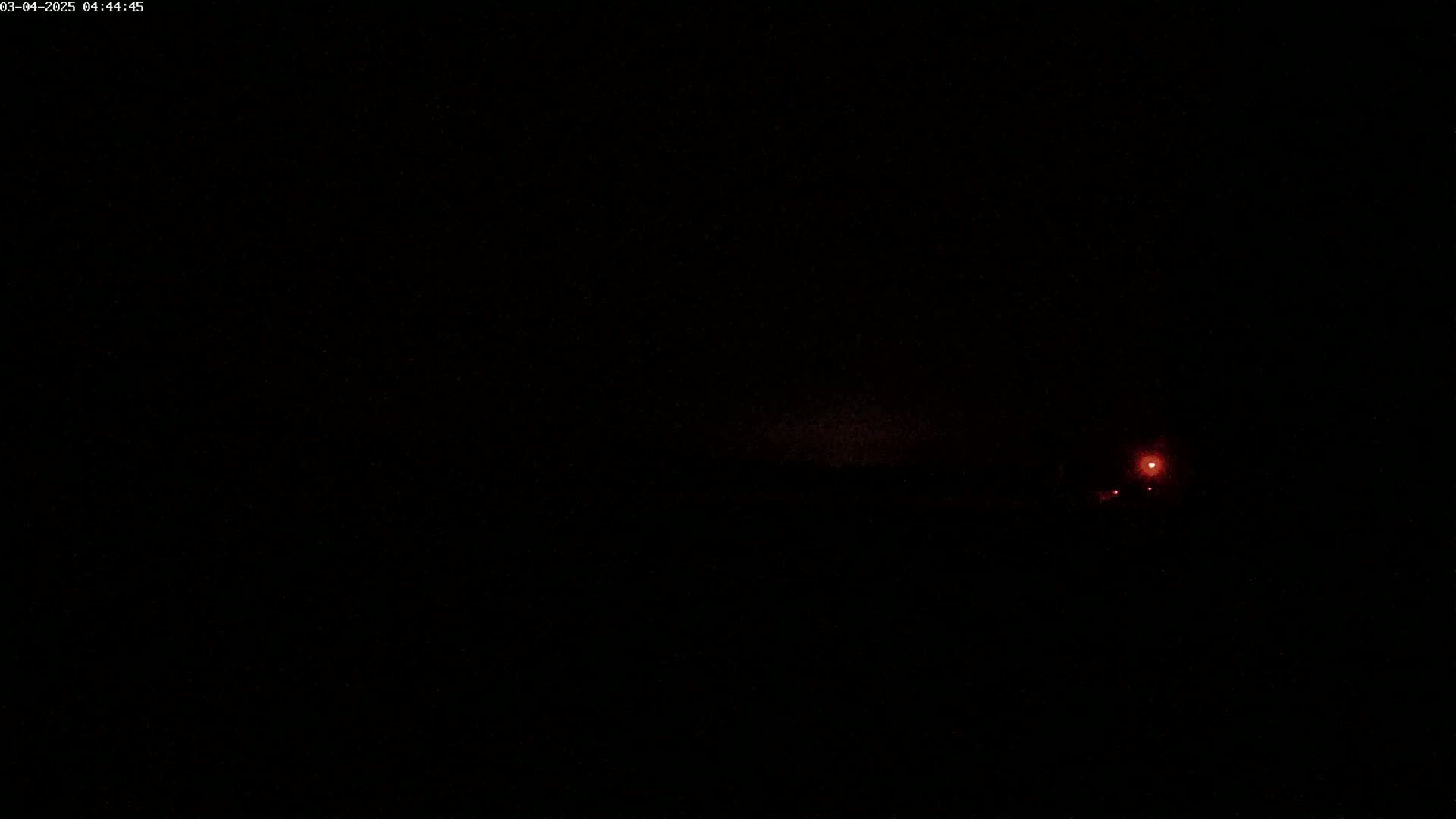 A dark, nighttime scene with a faint reddish light source in the distance.