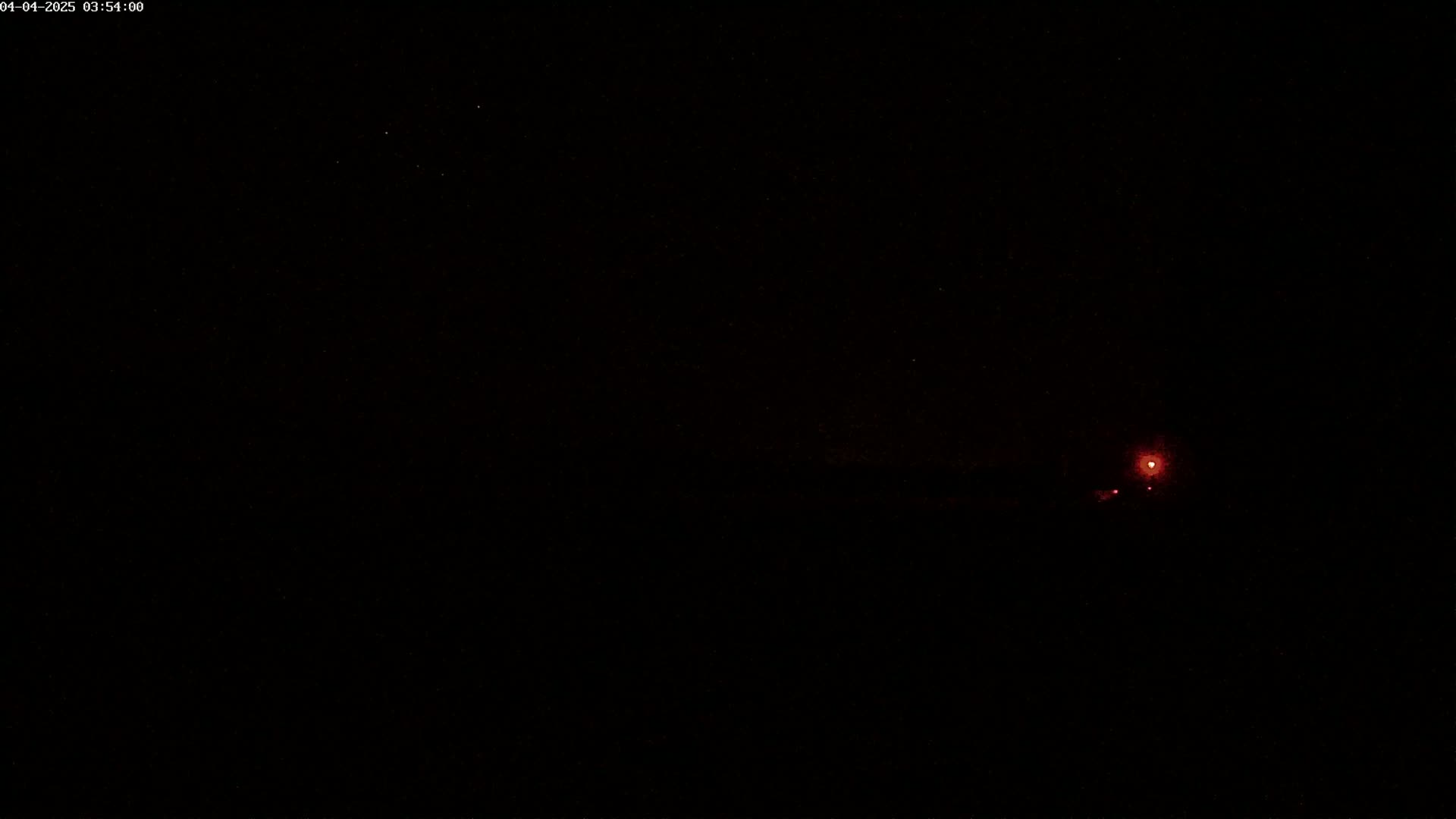 A small, faint red light is visible in the distance against a completely dark, nighttime sky.
