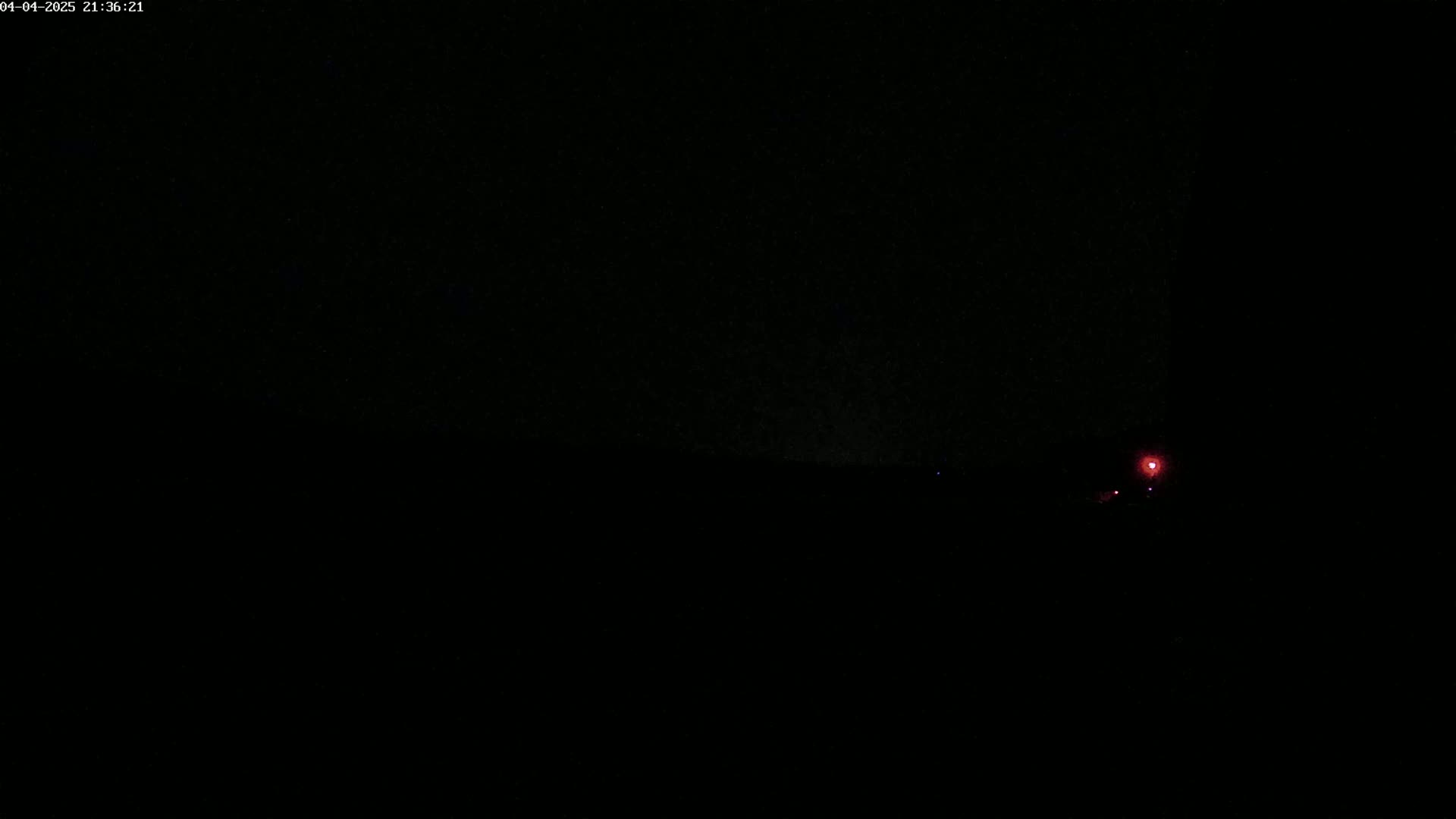 A dimly lit, dark landscape at night is shown with a single, small red light visible in the distance.