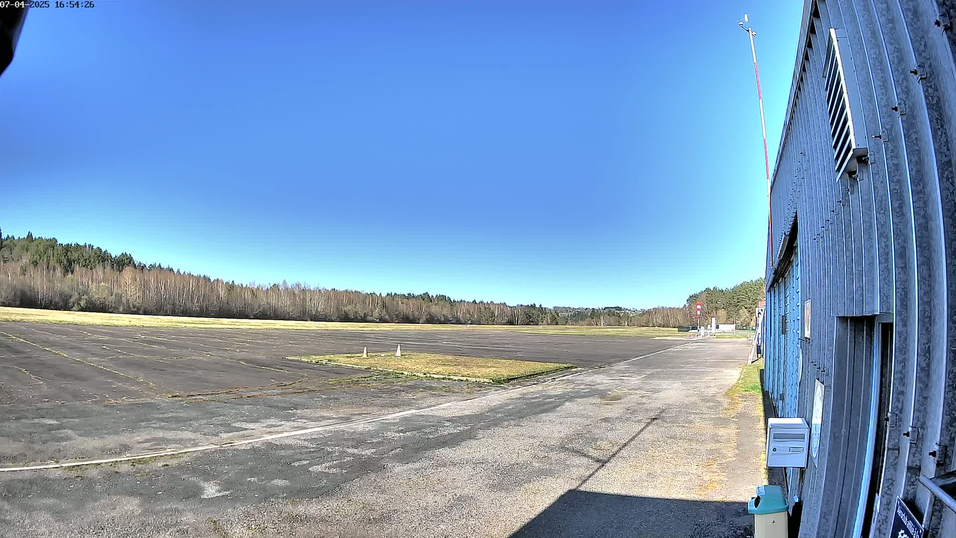 A paved airfield with a long, low building on the right, under a clear blue sky.