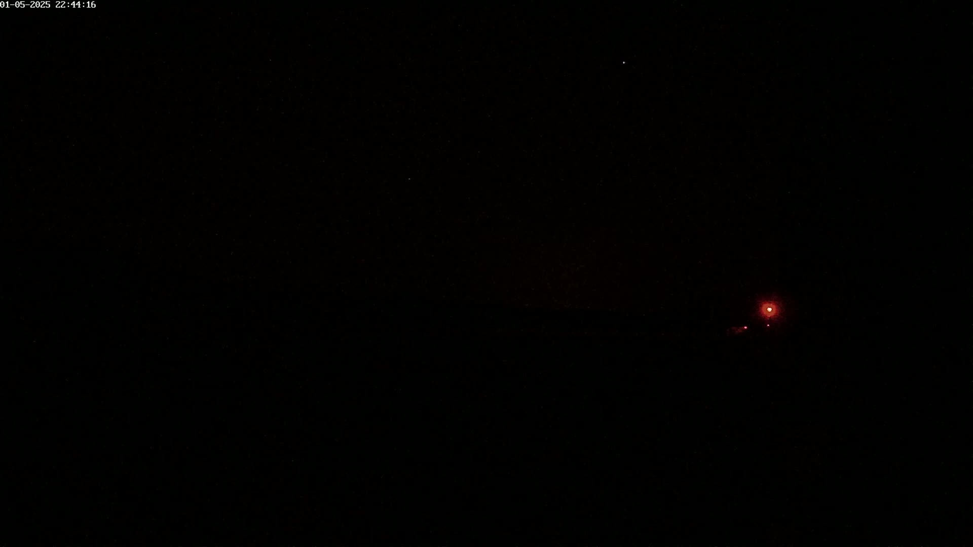 A nighttime outdoor scene shows two faint reddish lights in the distance against a dark sky.