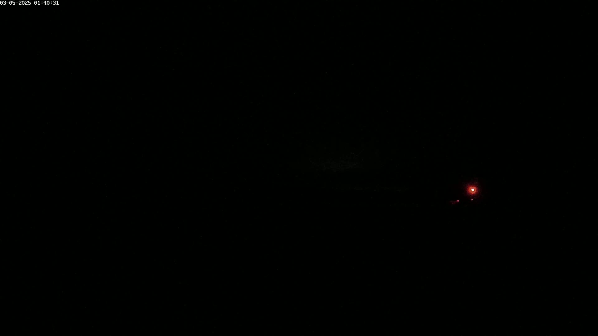 A dark, nighttime scene shows a faint red light in the distance.