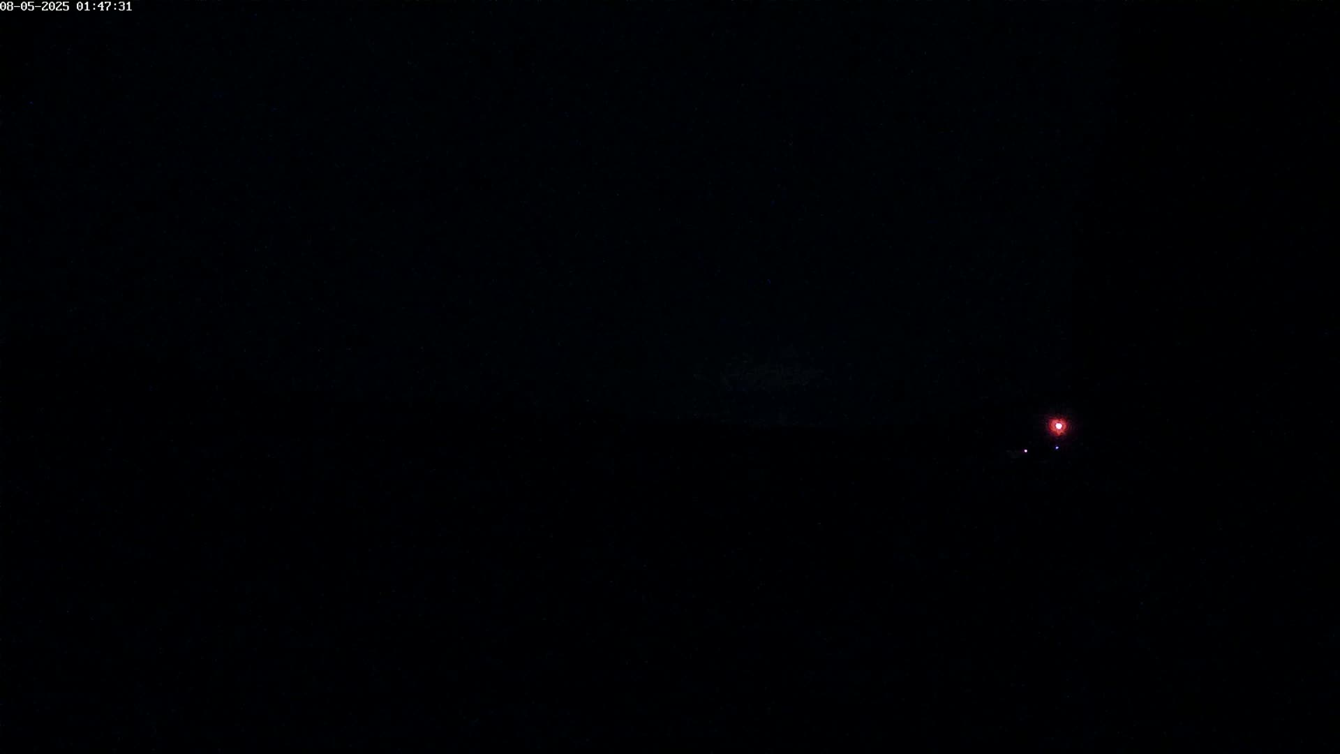 A dark, nighttime scene features a small, bright red light in the distance.