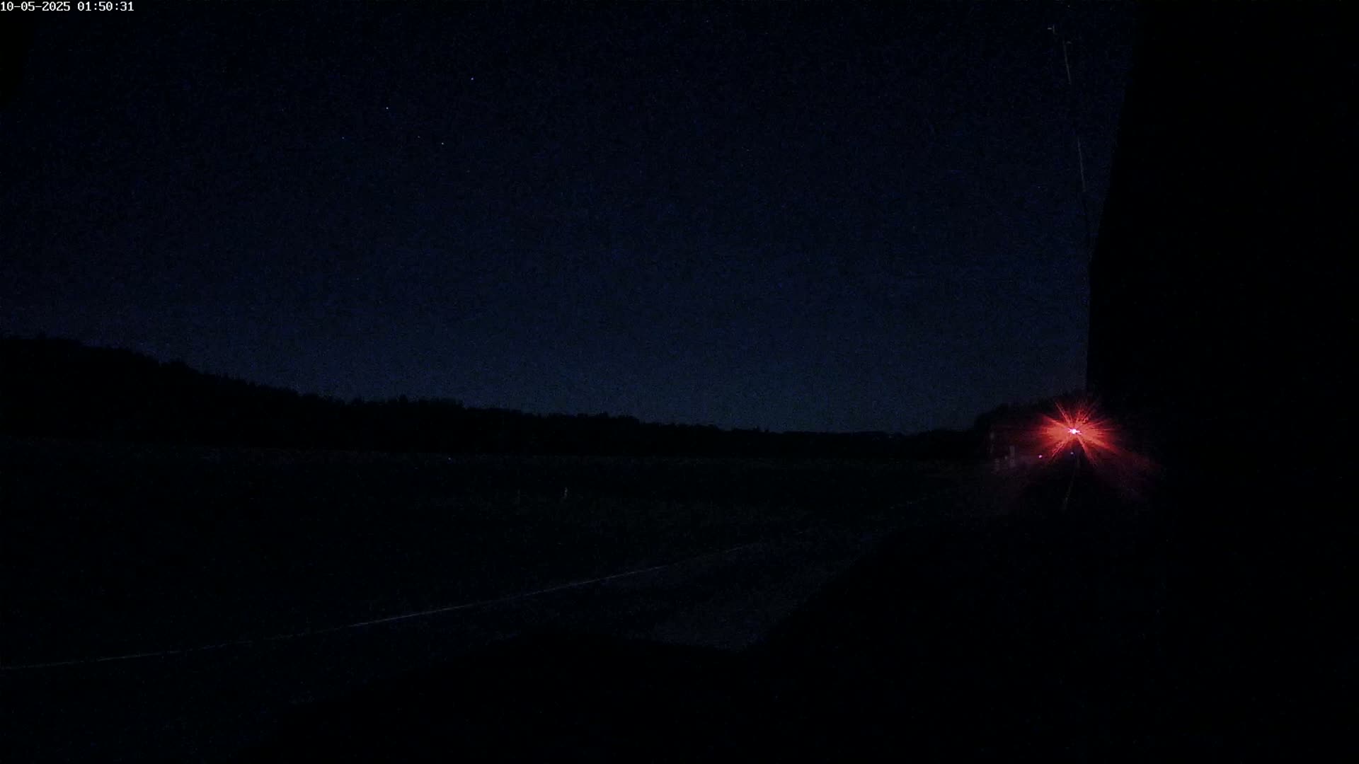 A dark, nighttime road with a distant red light visible, under a clear, starry sky.