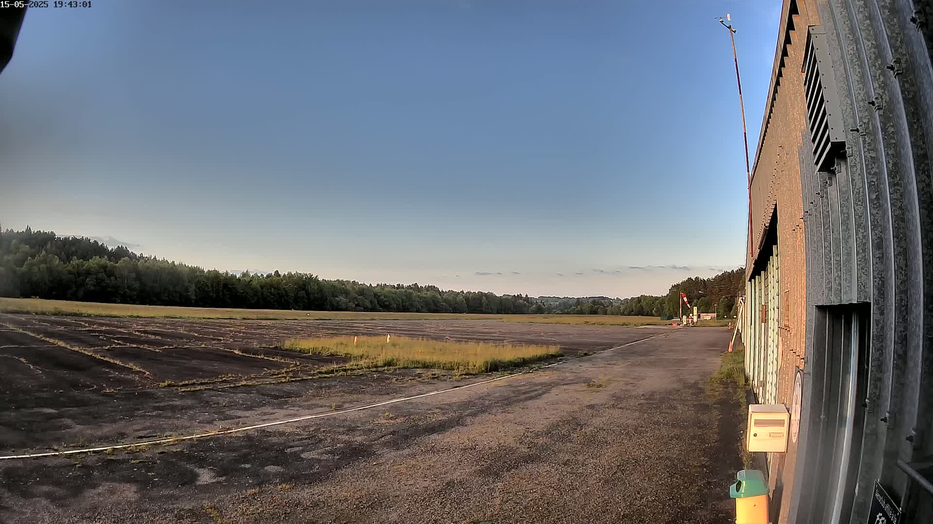 A mostly clear sky overlooks a grassy airfield with a long, weathered hangar to the right.