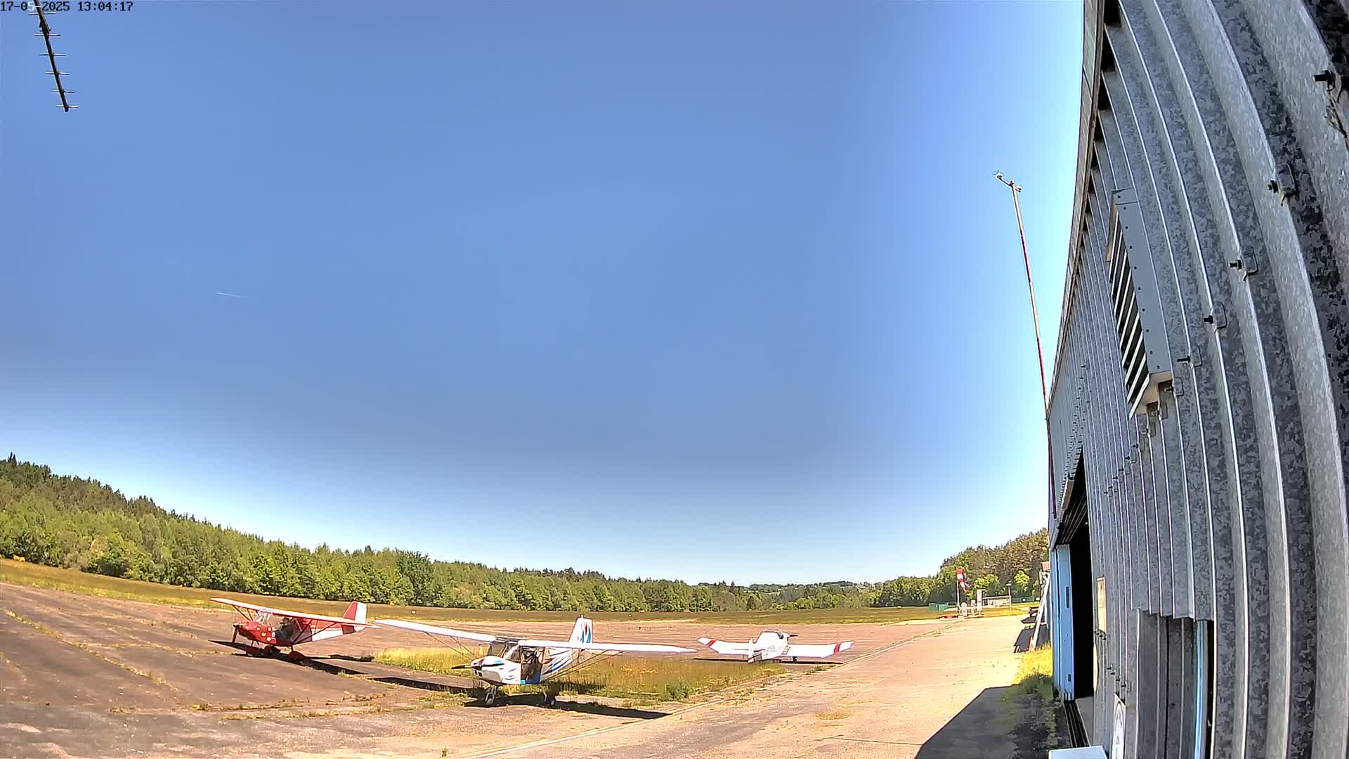 Three small airplanes sit on a tarmac beside a corrugated metal hangar under a clear blue sky.