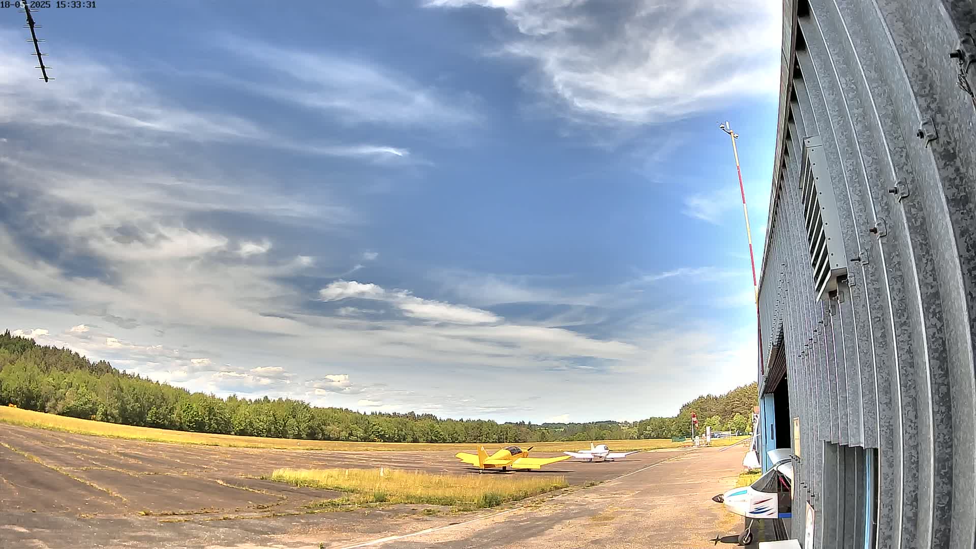 A small airfield with two small airplanes parked on a runway under a partly cloudy sky.
