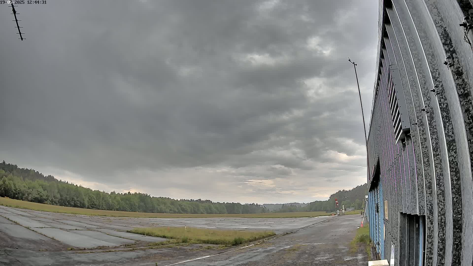 A large, empty, cracked asphalt area bordered by trees under a heavily overcast sky.