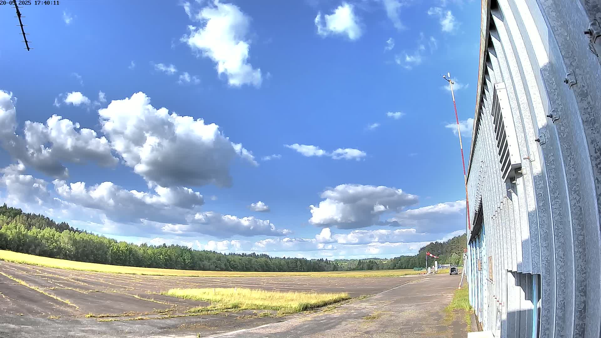 A partly cloudy sky overlooks a flat, grassy airfield next to a corrugated metal building.