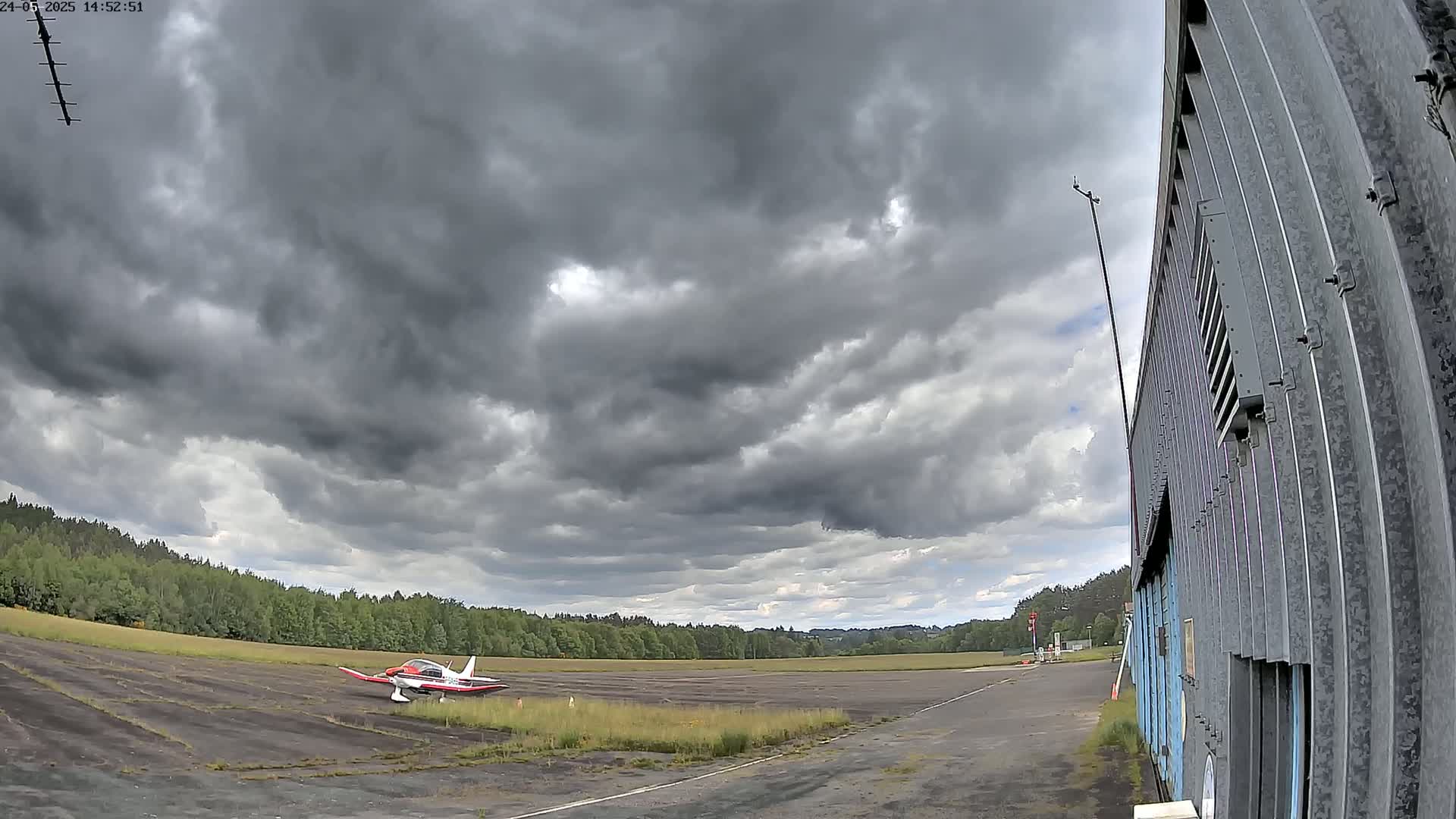 A small airplane sits on a tarmac next to a tall corrugated metal building under a cloudy sky.