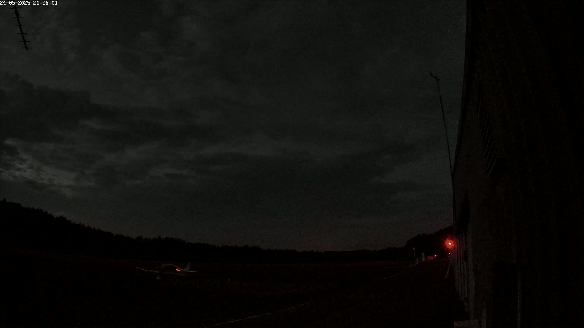 A small airplane sits on a dark tarmac under a mostly cloudy night sky.