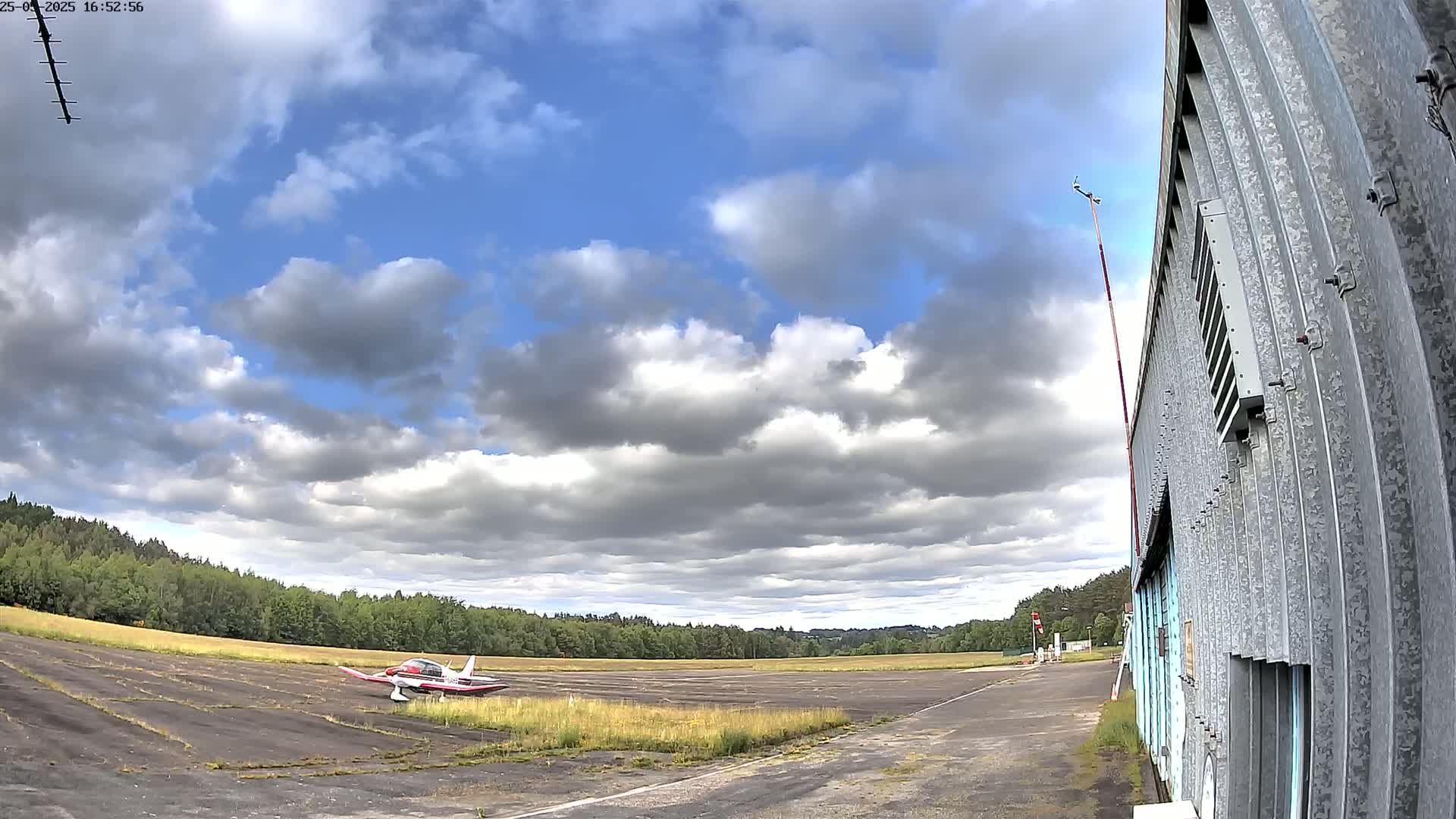 A small airplane sits on a tarmac next to a corrugated metal building under a partly cloudy sky.