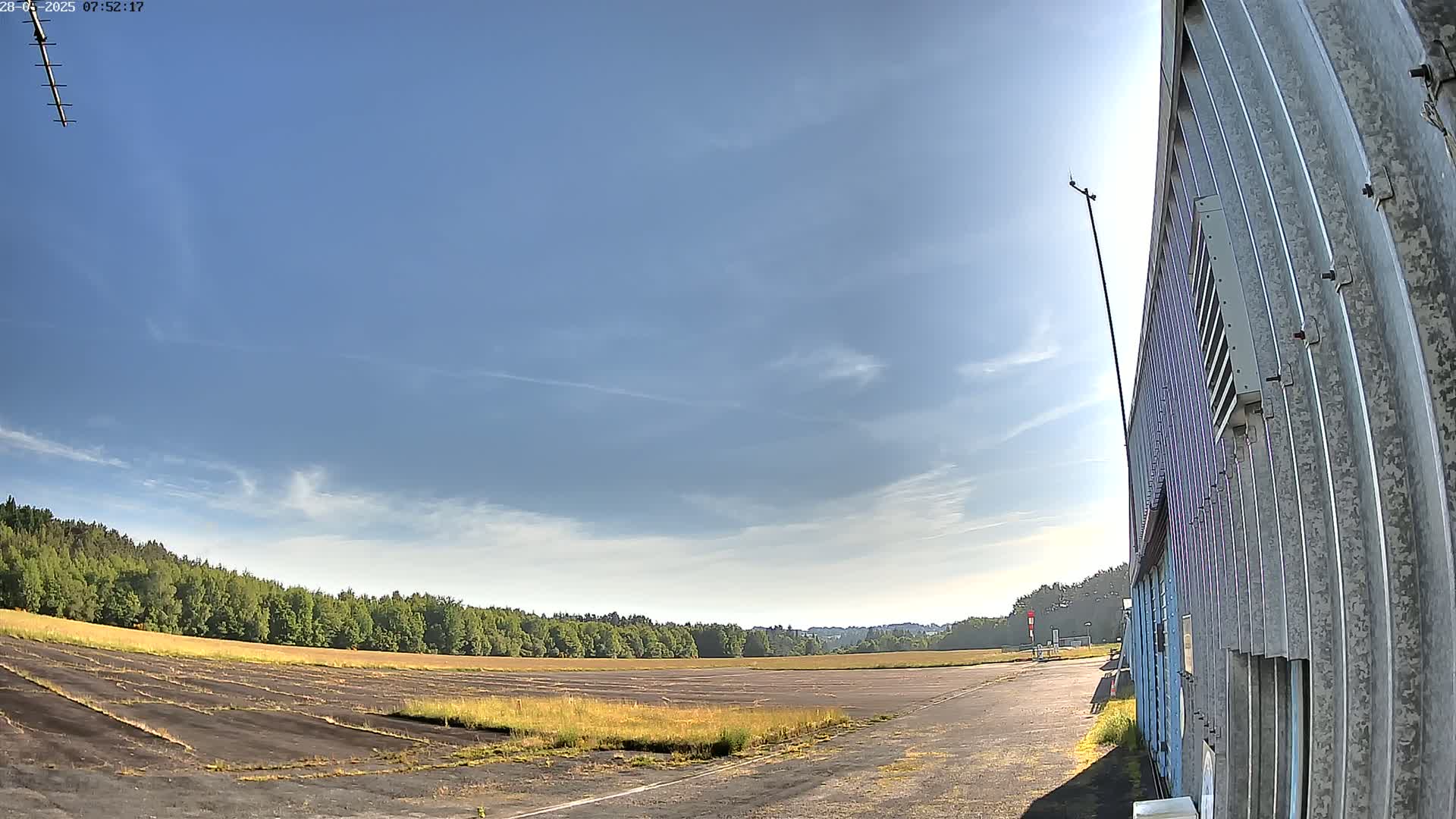 A mostly clear, bright blue sky over a paved, empty airfield next to a corrugated metal building.