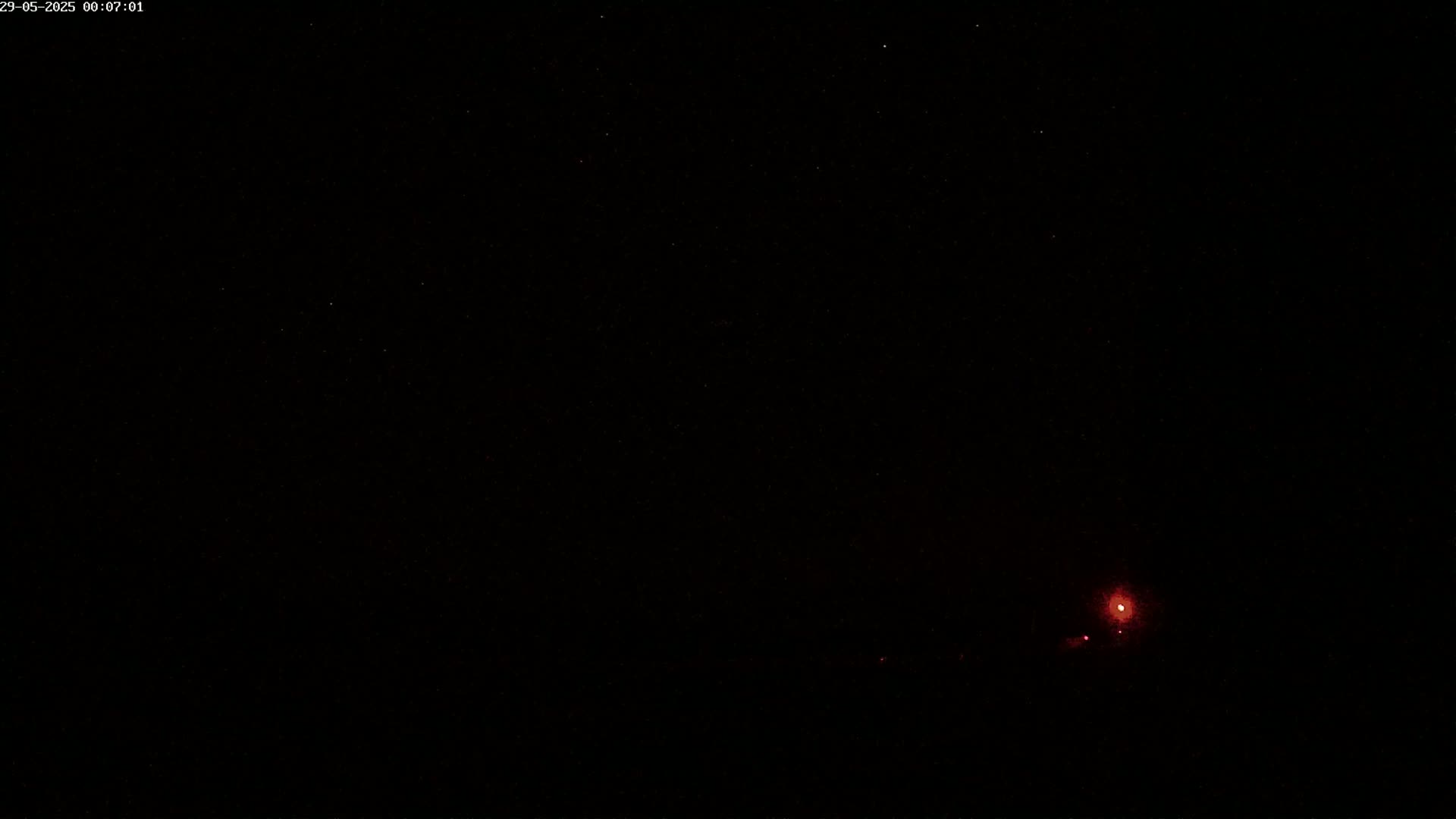 A nighttime scene shows a dark sky with a few faint stars and a small, reddish light in the distance.