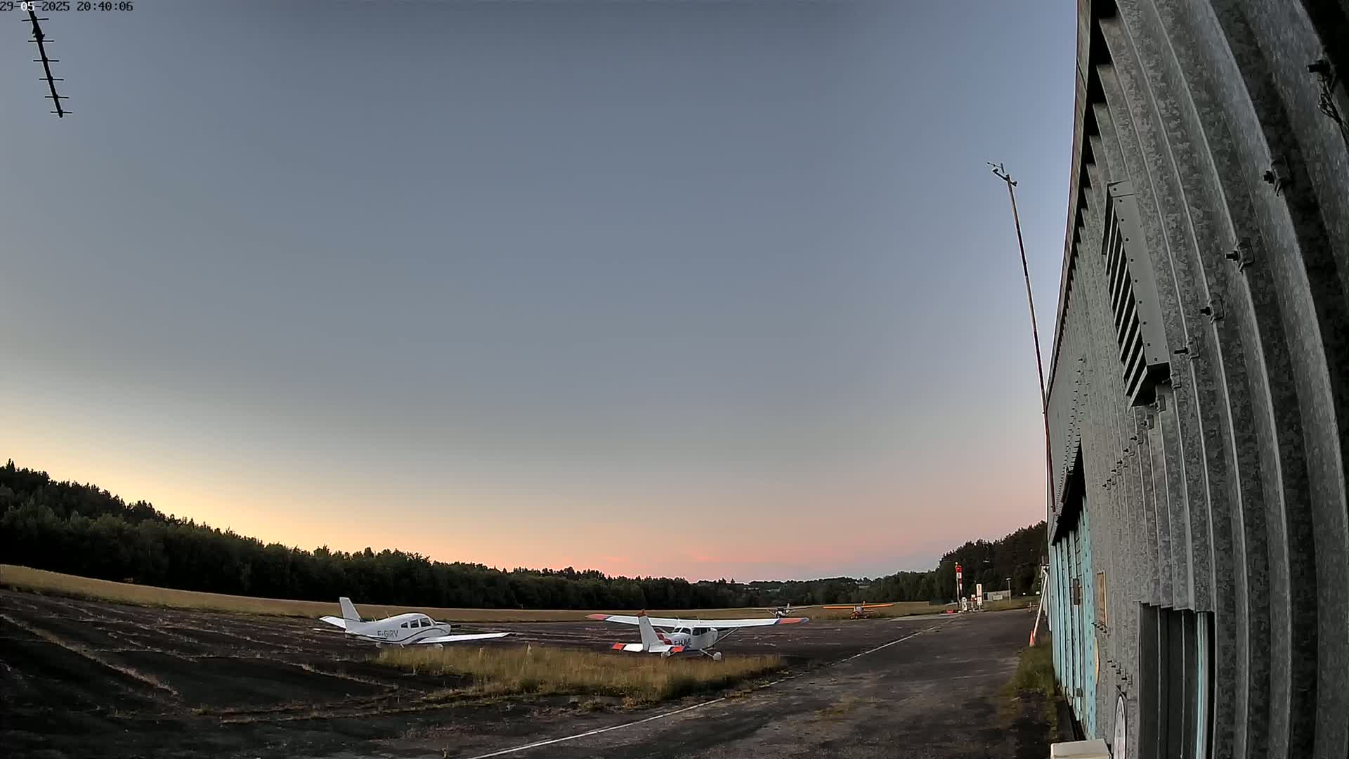 Two small airplanes are parked on an airfield at sunset under a clear sky.