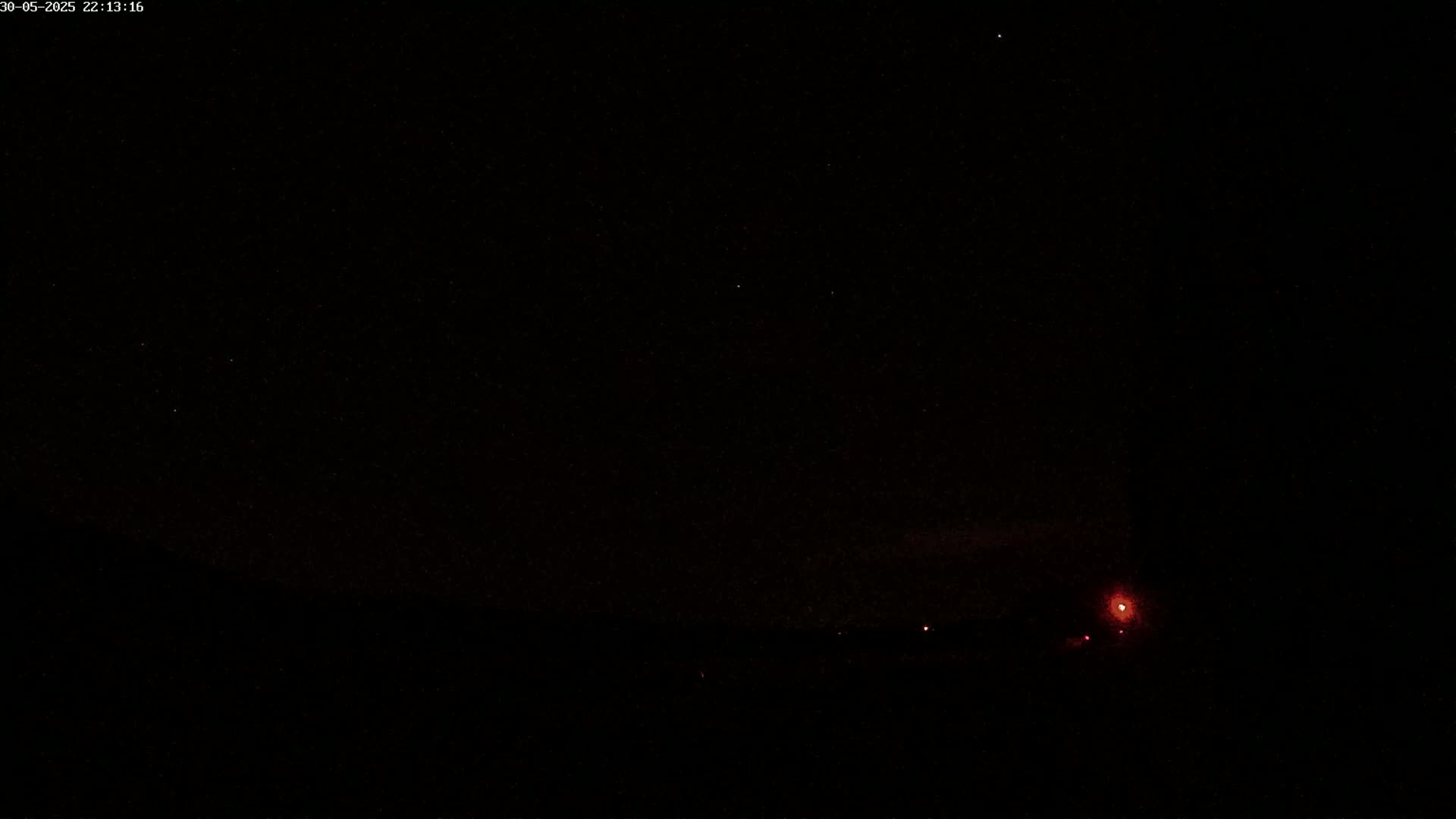 A dark night sky with a few faint stars and some distant red lights on the horizon.
