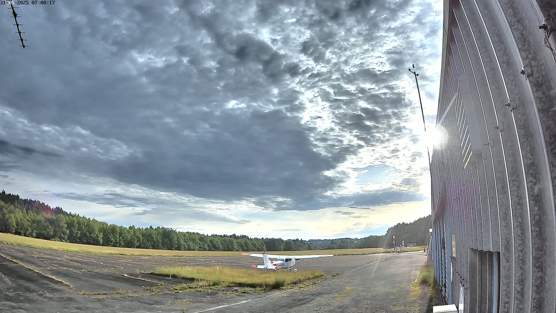 A small airplane sits on a tarmac next to a building under a partly cloudy sky.
