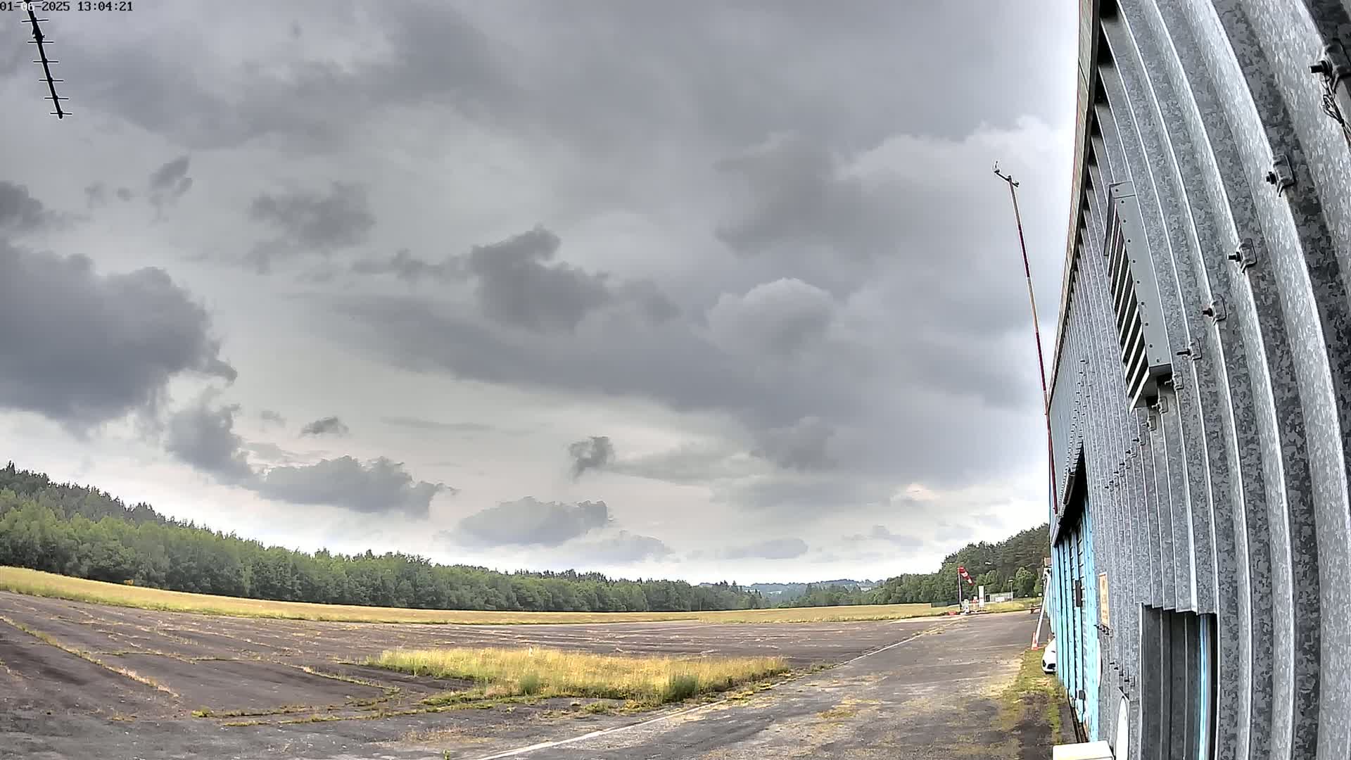 A mostly overcast sky looms over a flat, grassy airfield next to a corrugated metal building.