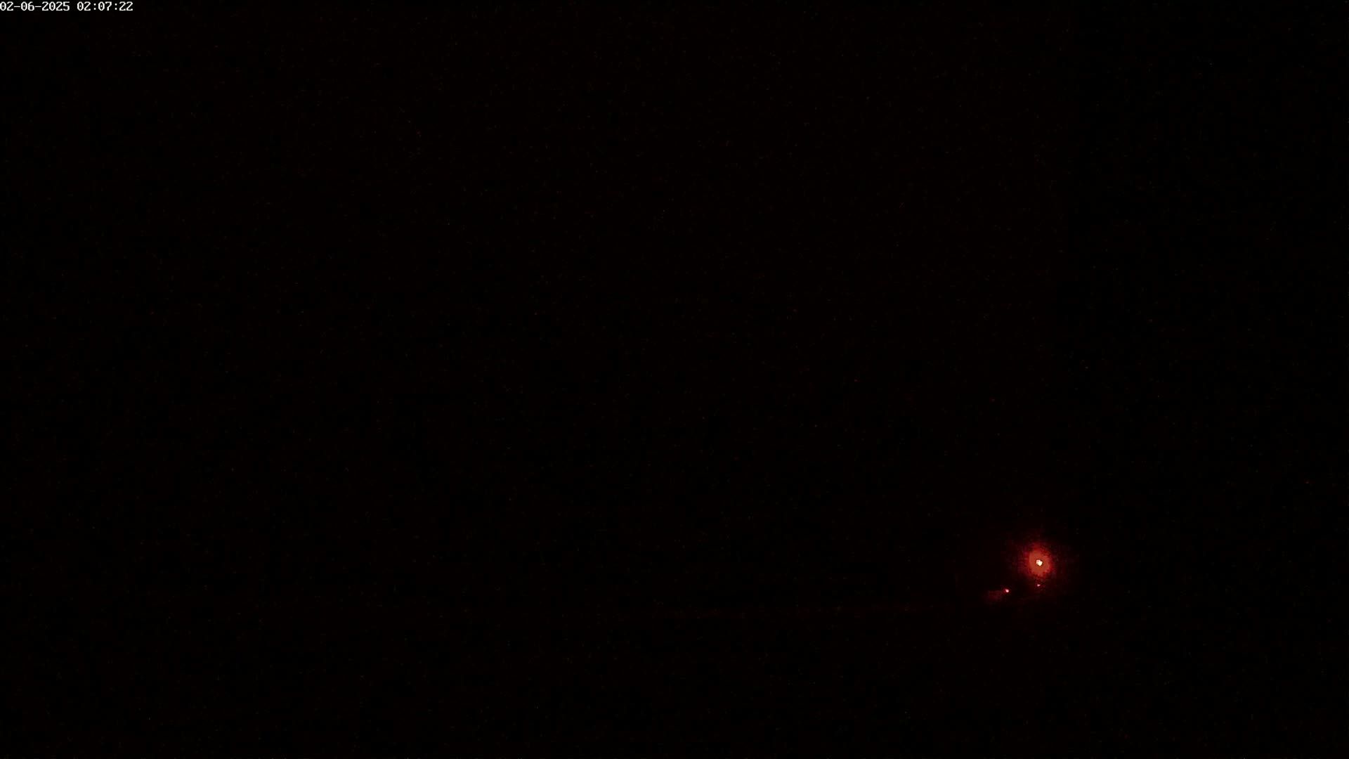 A dark, nighttime scene shows a faint reddish light in the distance.