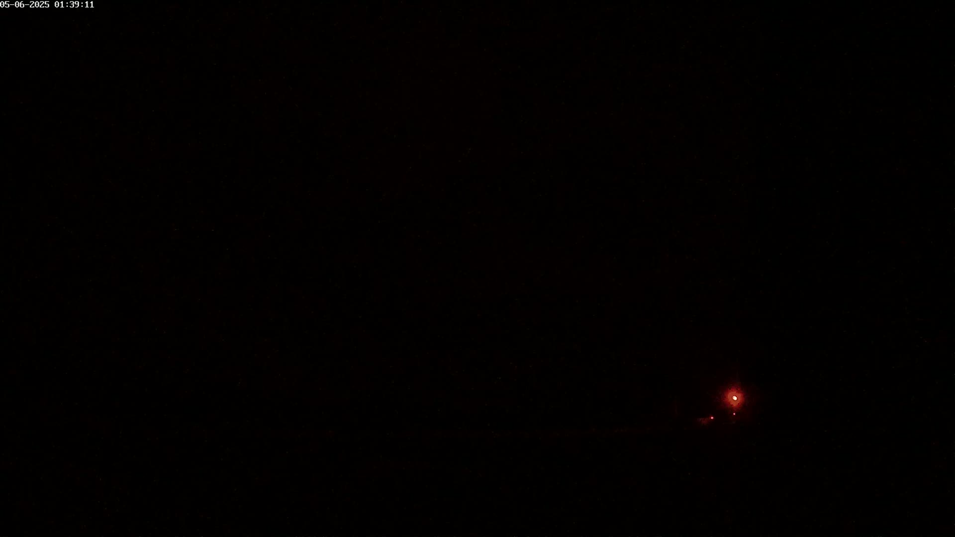 A small, faint red light is visible in the lower right corner of a completely dark, nighttime image.