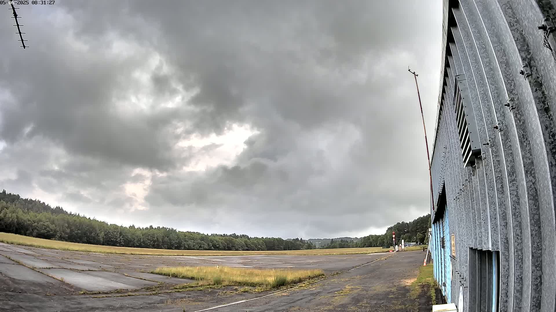 A mostly overcast sky hangs over a long, empty airfield next to a corrugated metal building.