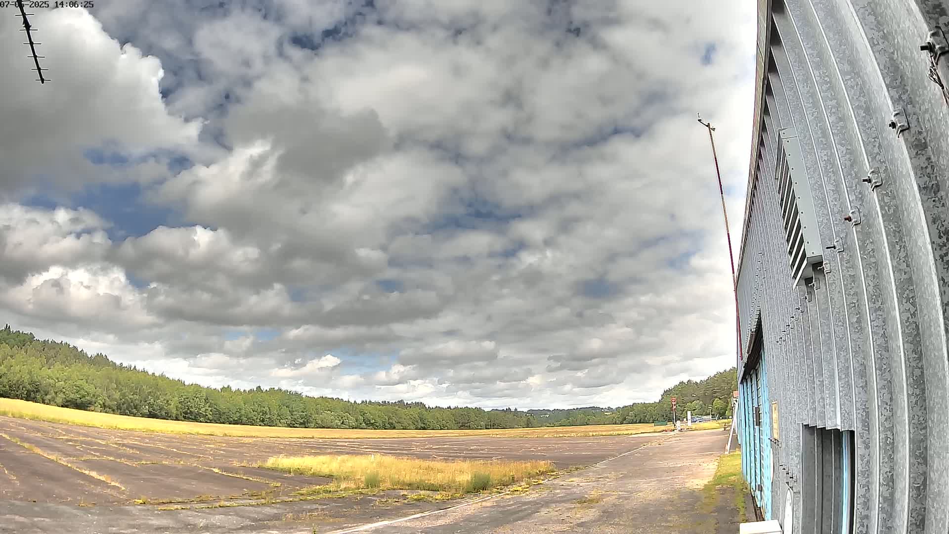 A mostly cloudy sky over a grassy airfield next to a corrugated metal building.