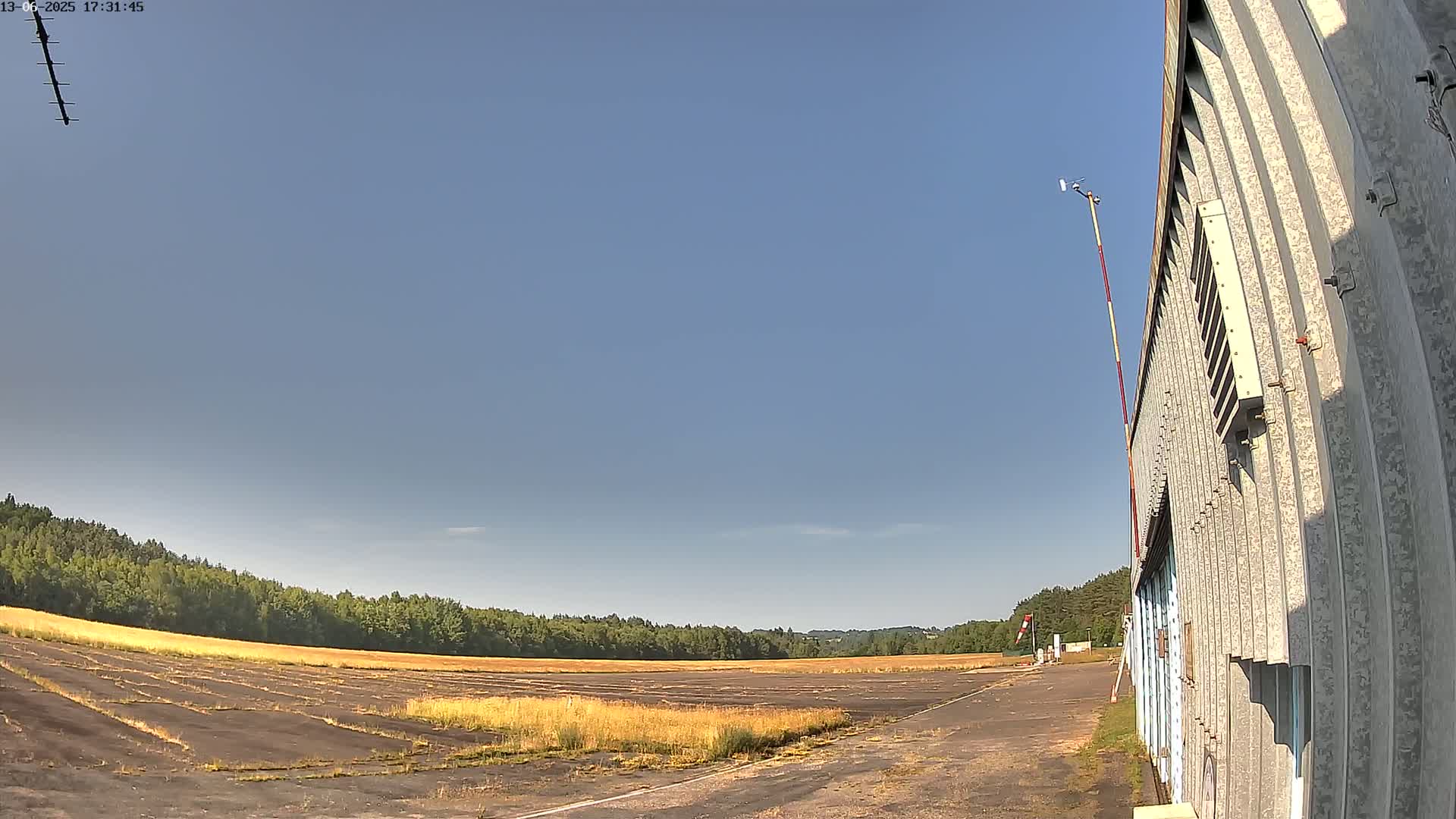 A long, flat, disused airfield stretches towards a line of trees under a clear blue sky.