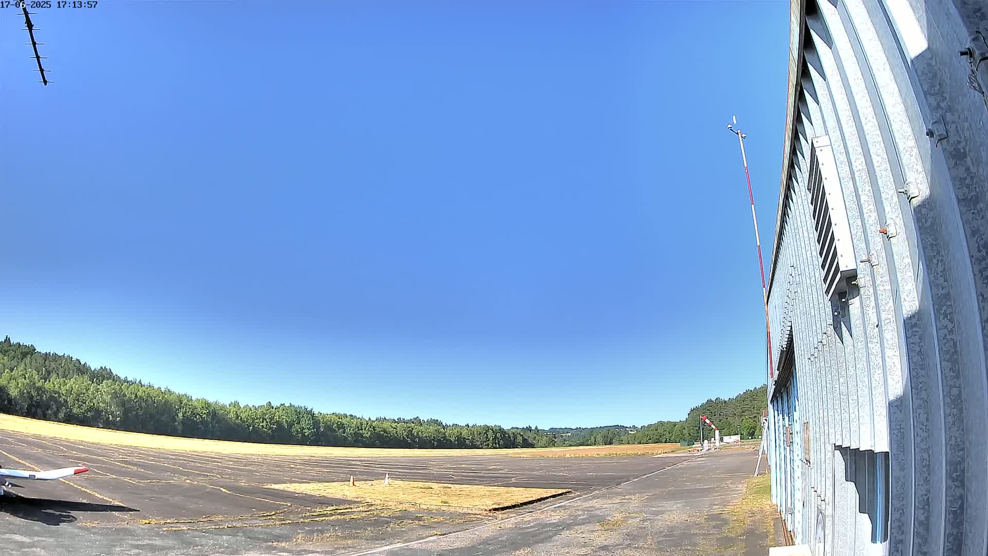 A small airplane sits on a tarmac next to a corrugated metal building under a clear blue sky.