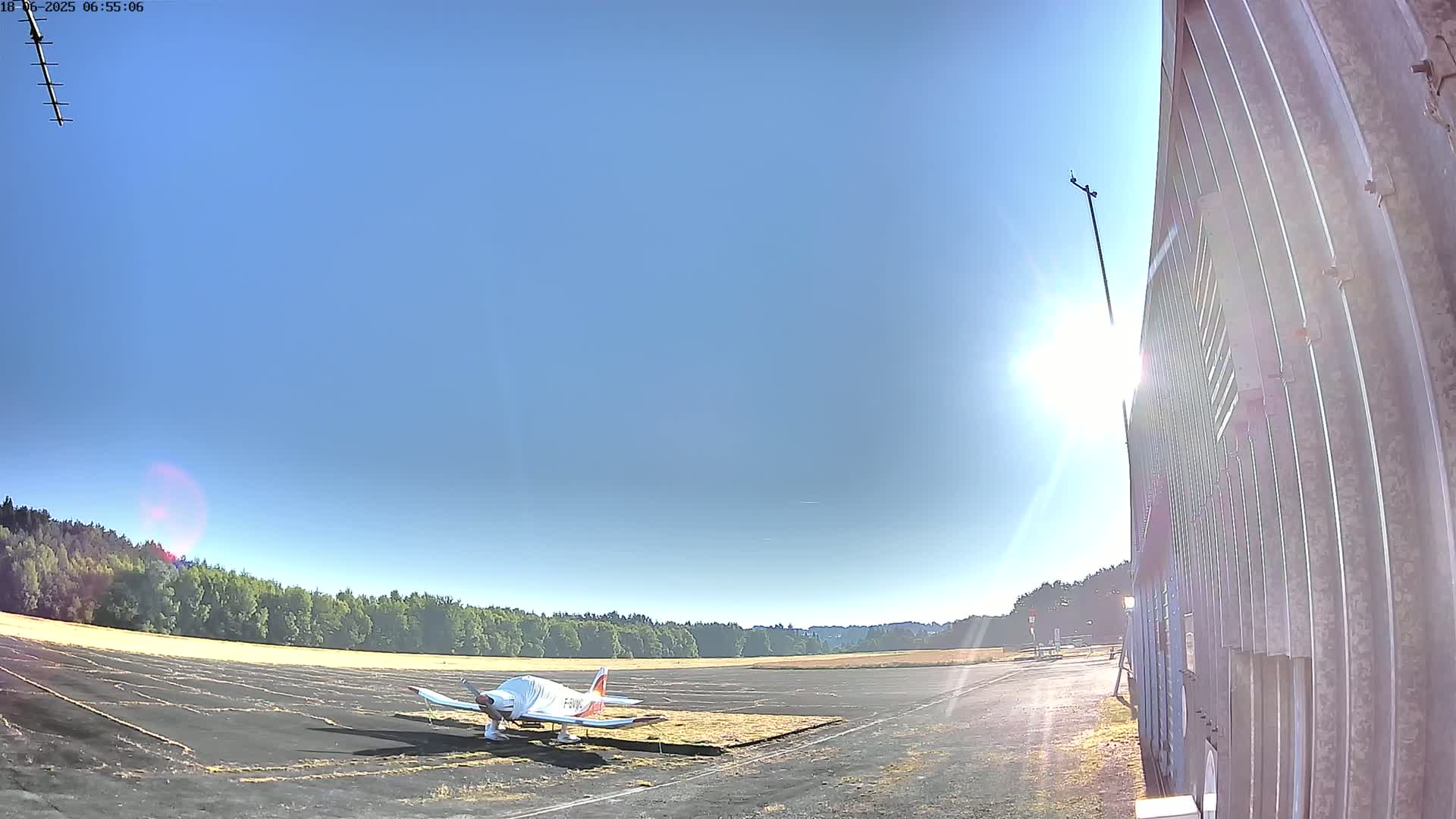 A small airplane sits on a tarmac next to a tall metal building on a sunny day.