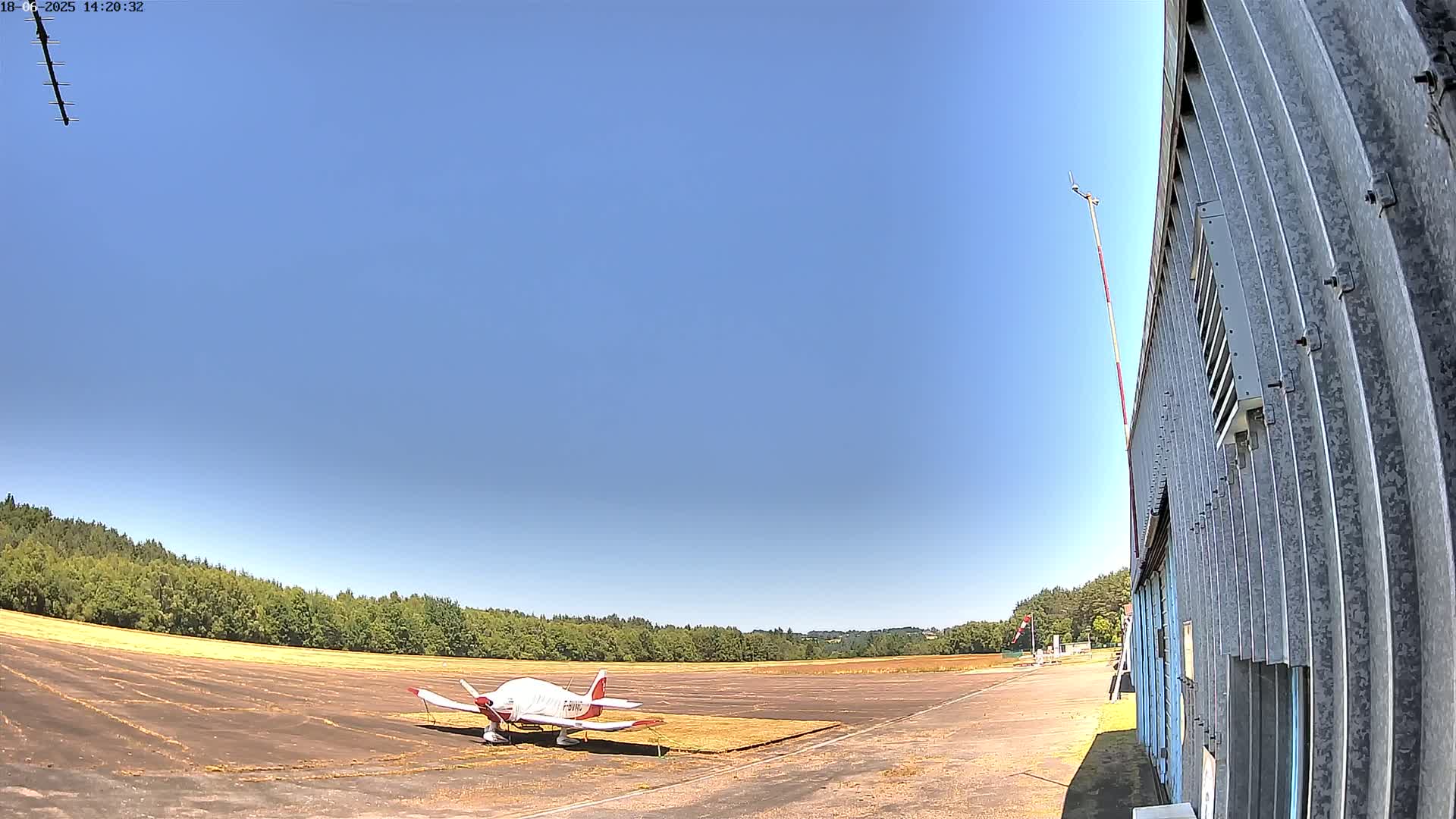 A small airplane sits on a tarmac next to a hangar under a clear blue sky.