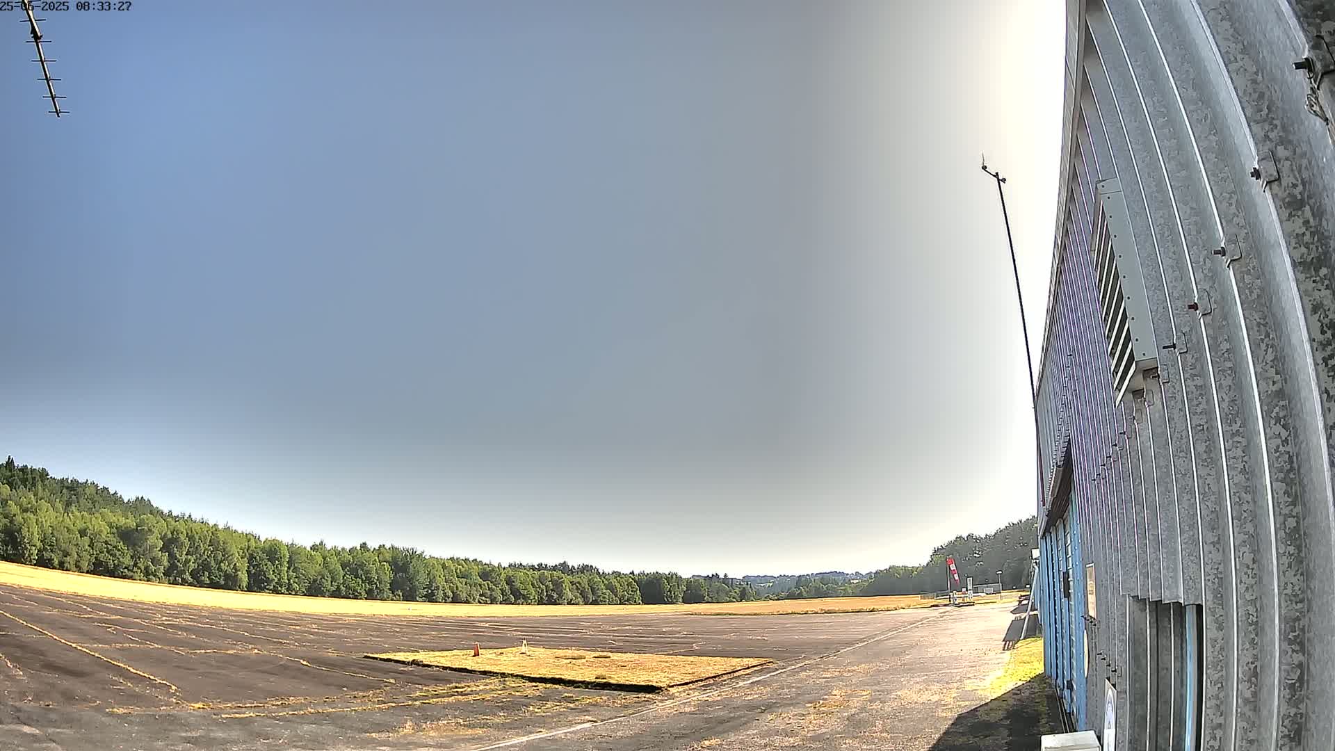 A paved area, possibly a runway or racetrack, extends towards a line of trees under a clear, sunny sky.