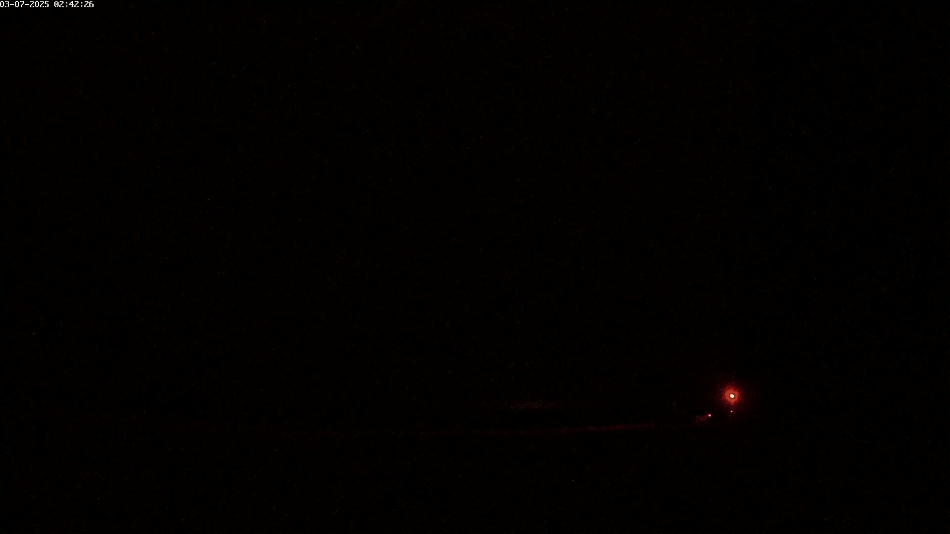 A faint red light is visible in the distance on a very dark night.