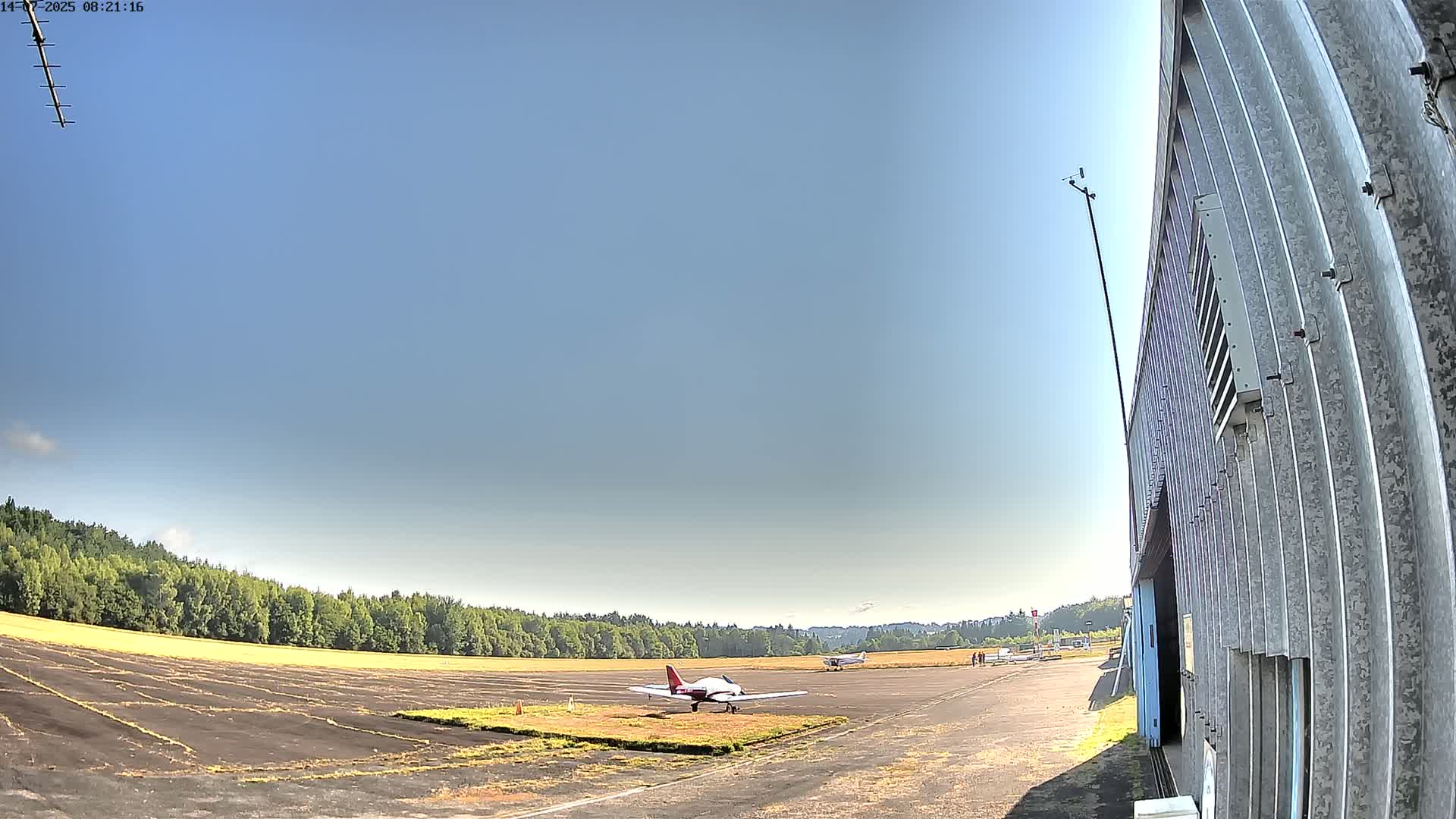 Two small airplanes sit on a tarmac next to a hangar, under a clear blue sky on a sunny day.