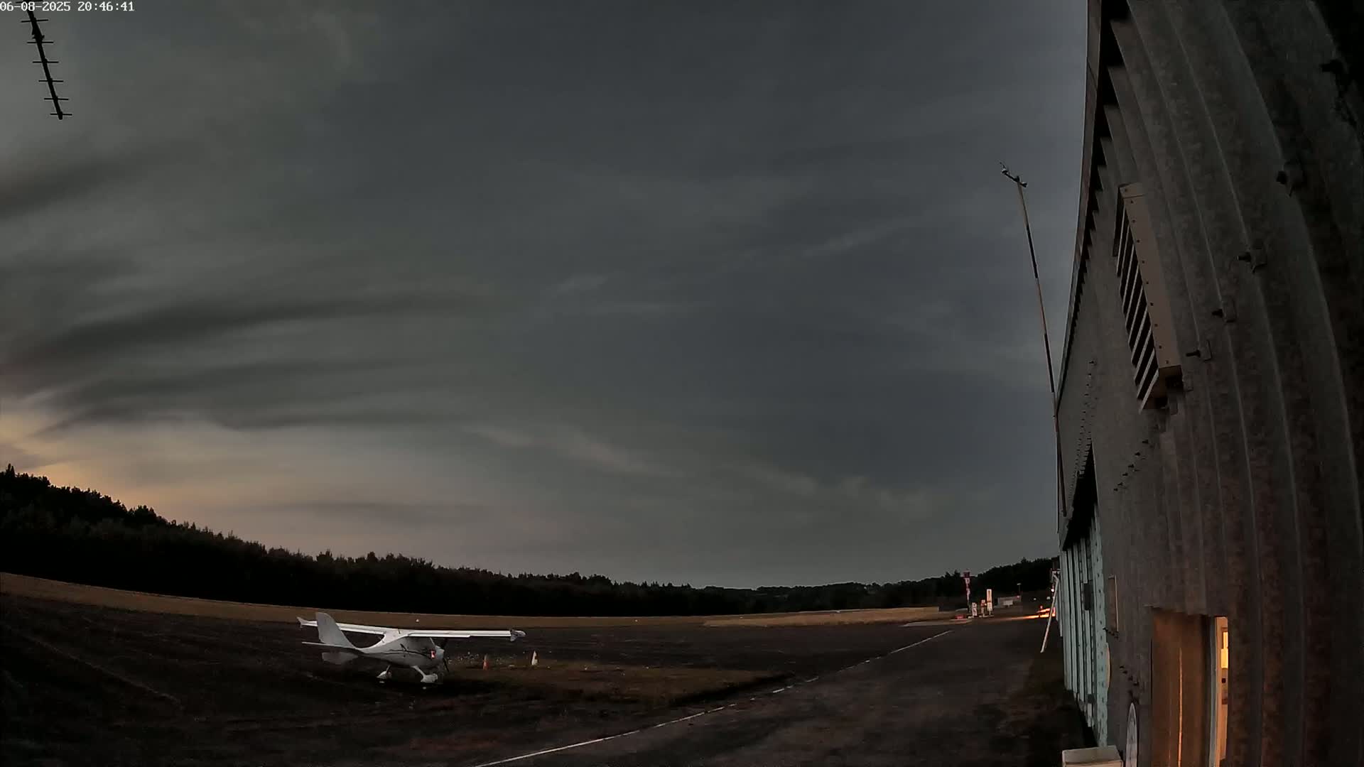 A small airplane sits on a tarmac next to a hangar under a dark, cloudy sky.